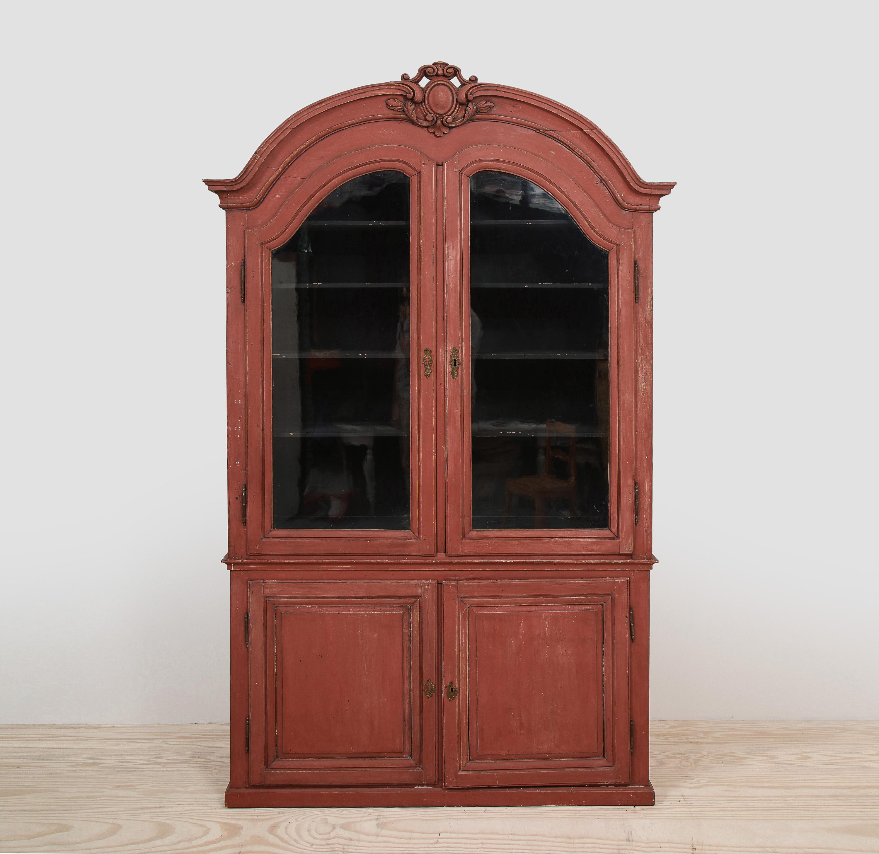 Swedish Rococo 18th century cabinet, origin: Sweden, circa 1760 - 1775, red exterior with glass doors revealing six shelves in a dark grey/blue interior and two cabinets below. Beautiful proportions with hand-carved center cartouche. 

The purity of