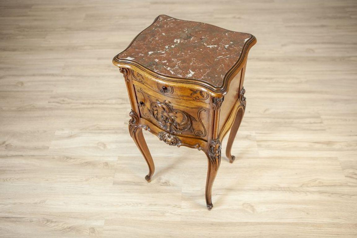 Rococo Walnut Night Stand From the Turn of the Centuries With Marble Top

A Rococo-style night stand with a marble top, a drawer, and a door. The item is adorned with floral-themed woodcarvings. The piece is made of walnut wood and veneered, fully