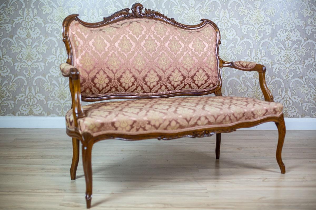 We present you a small double sofa with a lightweight wooden frame and a softly upholstered seat and a backrest. All is from the Interwar Period.
The bent legs and backrest frame are decorated with carved patterns with fluting and the rocaille motif