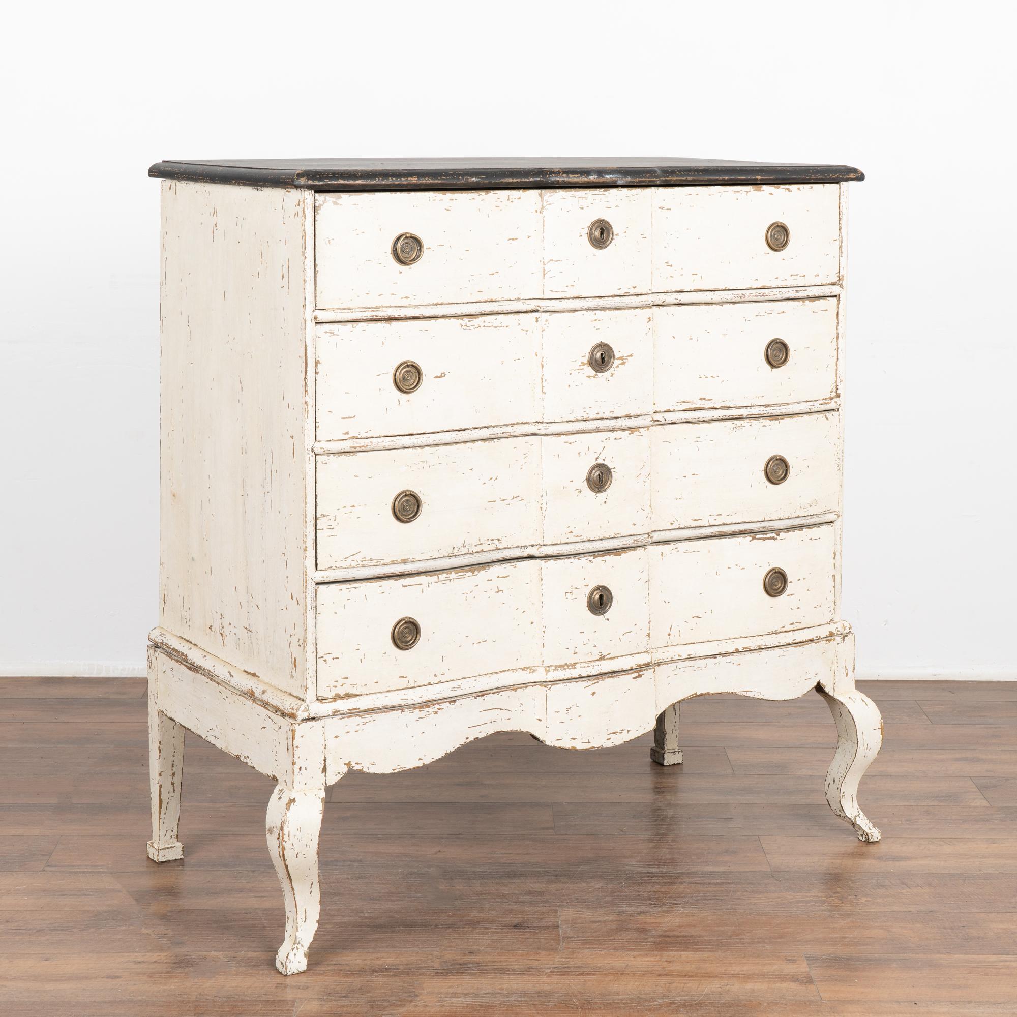 This antique rococo chest of drawers from Denmark features a serpentine front, brass hardware pulls and an exceptional (newer) white painted finish with contrasting black painted top.
Curves accentuate the skirt and front cabriolet legs. 
The