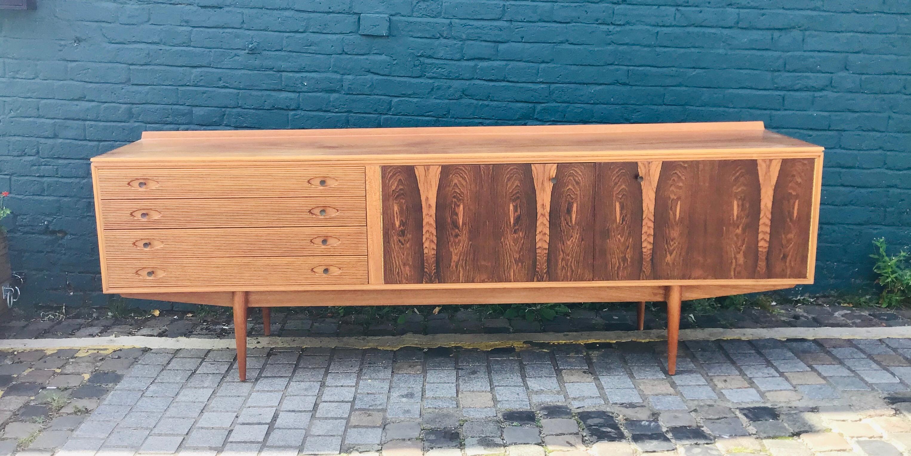 Stunning rosewood grain pattern to doors and top, and reeded solid teak drawer fronts with turned brass handles.

- Elegant styling, a statement piece.

Robert Heritage is synonymous with great British design. The Hamilton sideboard, an award