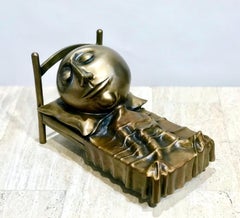 Slumber, escultura en bronce de Rodger Jacobsen hombre delgado durmiendo en la cama con cabeza grande