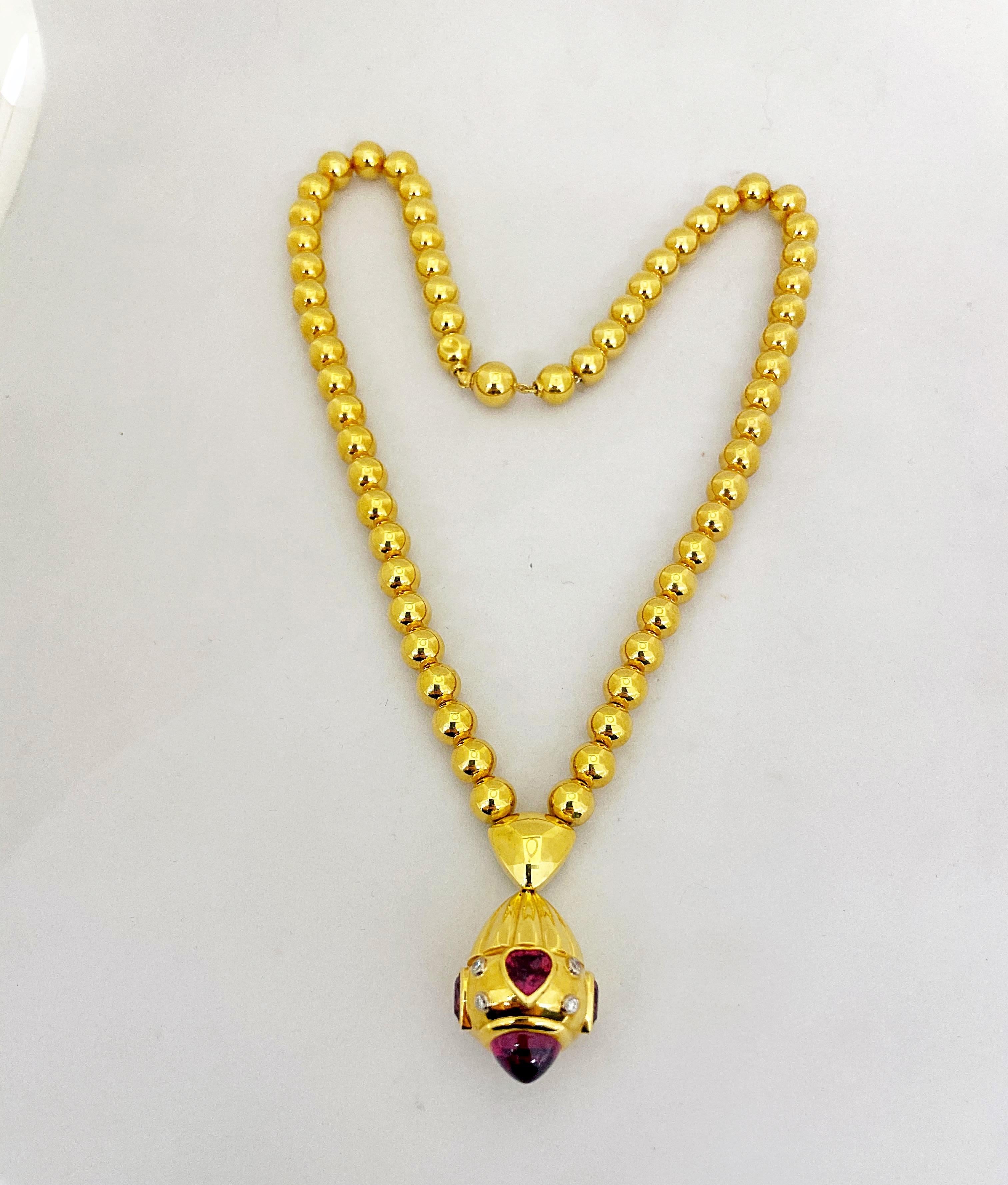 Rodney Rayner is known for his unique styling and use of beautiful color combinations. This 18 karat yellow gold necklace is a perfect example of his work. 
This necklace is designed with a strand of 7 mm gold beads. A drop pendant, set with heart