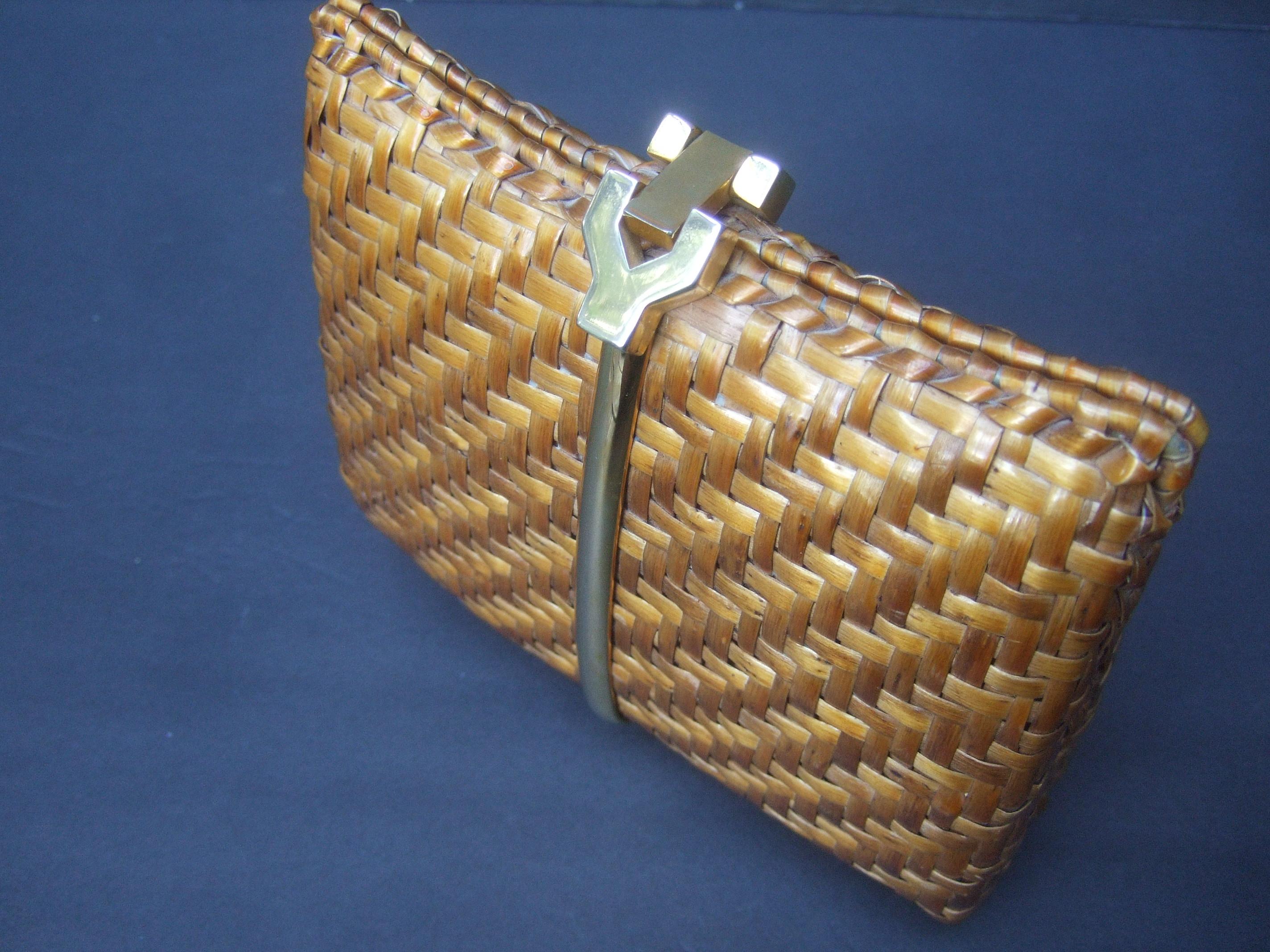 Rodo Italy woven rattan wicker clutch bag c 1980
The light brown compact size wicker clutch is designed with a sleek gilt metal band that runs thru the center of both exterior sides 

The interior is lined in light brown vinyl stamped: Rodo Italy