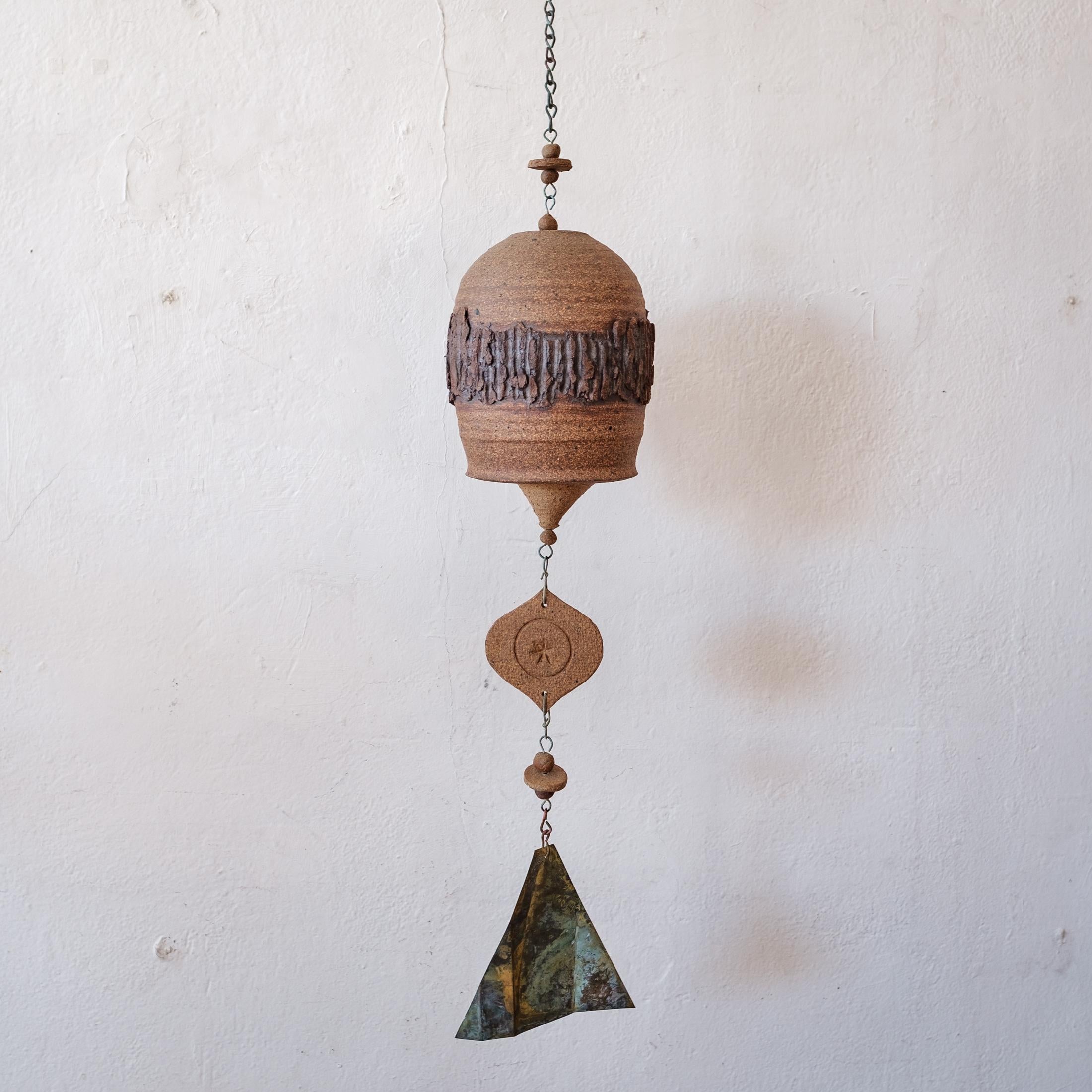 Hanging ceramic bell or chime by California ceramic artist, Roger Bailey. Textured wheel-thrown stoneware body with handbuilt hanging elements. Nice patina on the chain and wind catcher. Incised signature. 

The total height including chain and