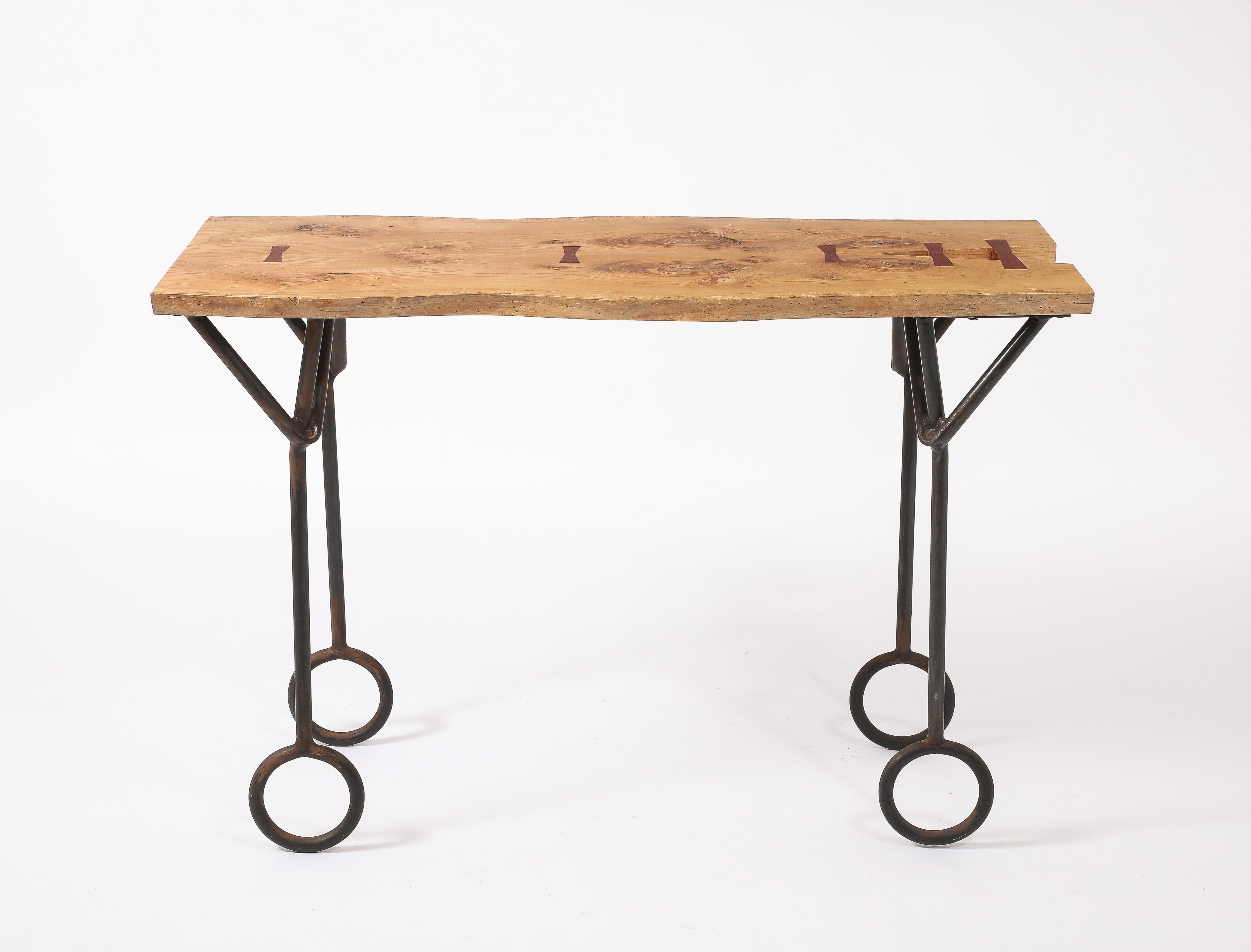 A console in wrought iron with a live edge top linked by walnut butterflies, the legs end in large circles

