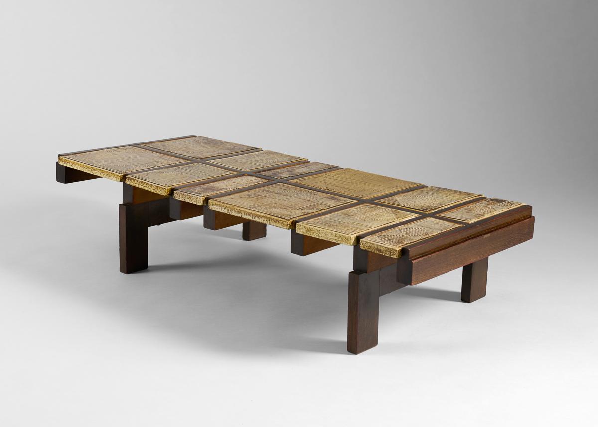 A coffee table by the great French designer Roger Capron, featuring a criss-crossing polished wood frame, and a ruddy ceramic tile top that extends on one side more than on the other with a unifying lack of symmetry.