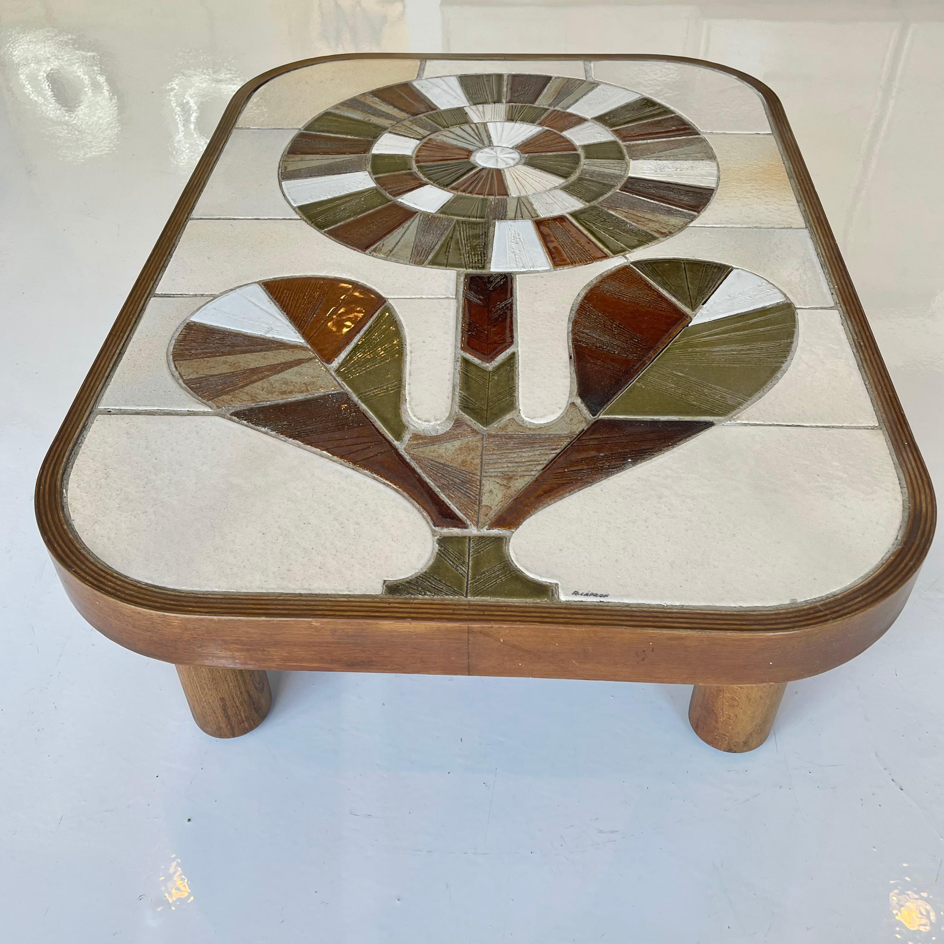 Beautiful ceramic coffee table signed by Roger Capron. Tiles of an array of different shapes, colors and textures come together on this coffee table to create a stunning mosaic table top. Fantastic rectangular shape on cylindrical Mahogany wood legs.