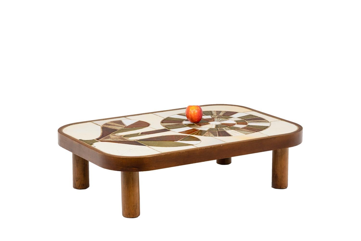 Roger Capron, signed.

Coffee table in wood standing on four cylindrical legs. The tray is inlaid with different pieces of green, white, cream-color and red enameled ceramics forming the stylized drawing of a flower with its stem and two leaves.