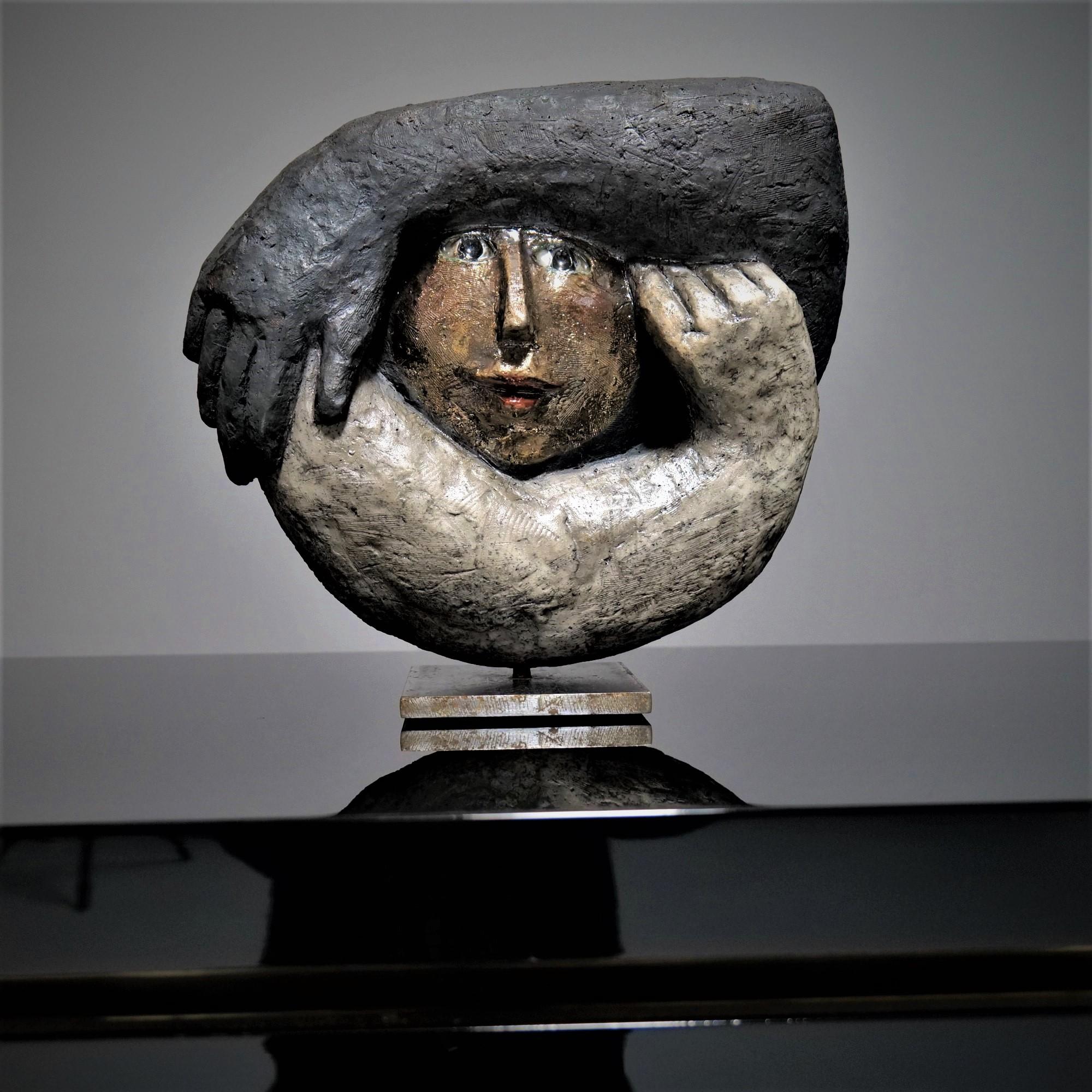 The object was exhibited in Stuttgart in 2002 as part of an exhibition called “The Poetry of Ceramics”.
The double-sided ceramic called “Kokon” shows on the raised side two arms lying in a circle, which frame a golden face.
The opposite side, kept