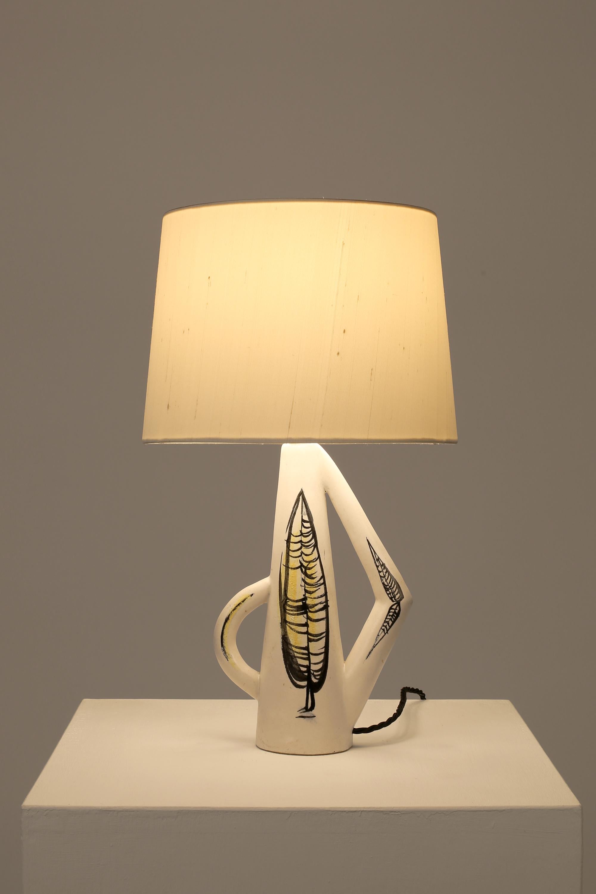 A white glazed ceramic table lamp of abstract urn-like form with foliate motifs, signed ‘Capron 512’. French, c. 1950s. Supplied with a bespoke off-white dupion silk shade.
