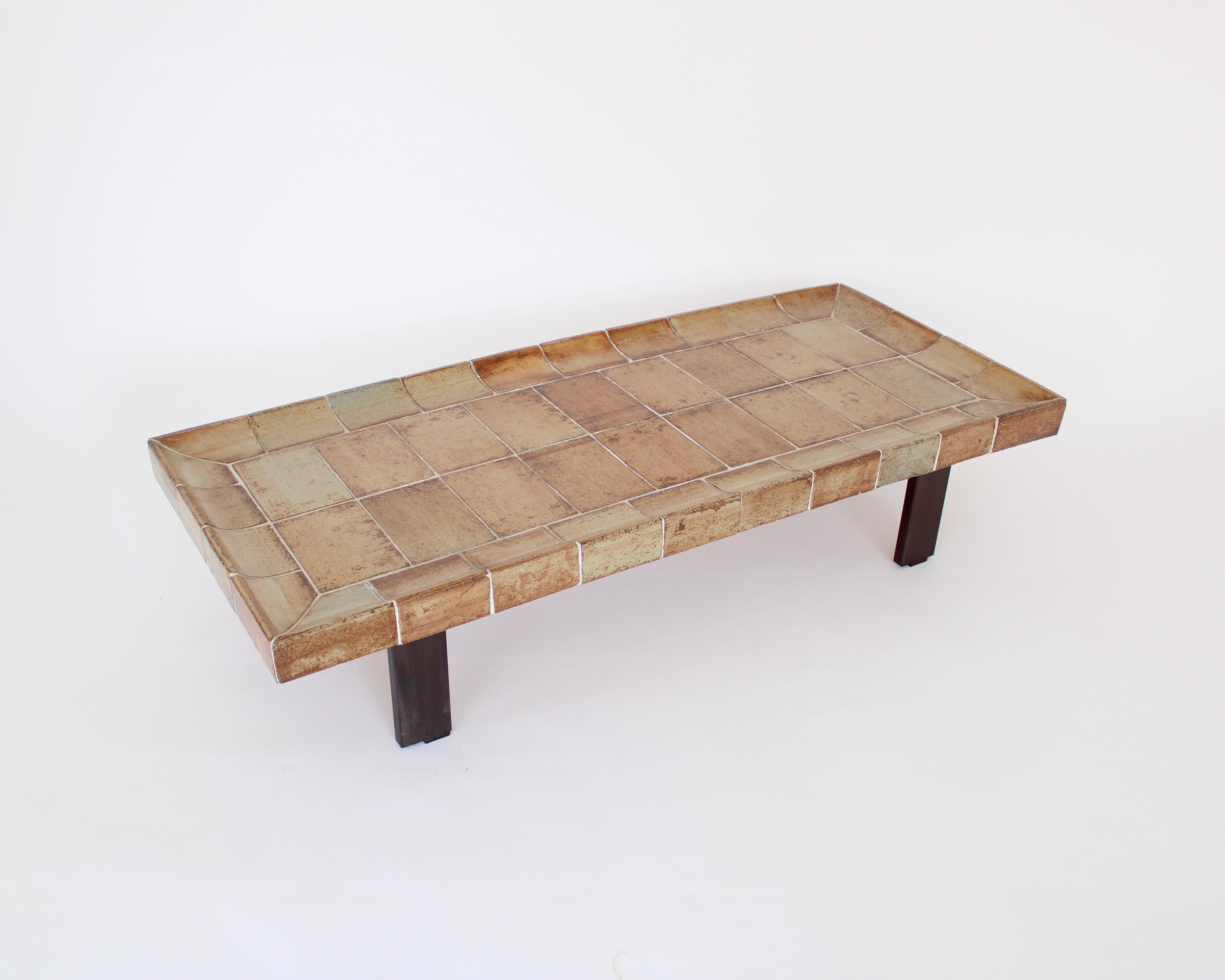 Roger Capron French ceramic tile coffee table model Cuvette. This table is composed of tiles that each exhibit the strong influence of the fire in the kiln and vary in colors of warm caramel, pale brown, beige, tan. The tiles have a central motif