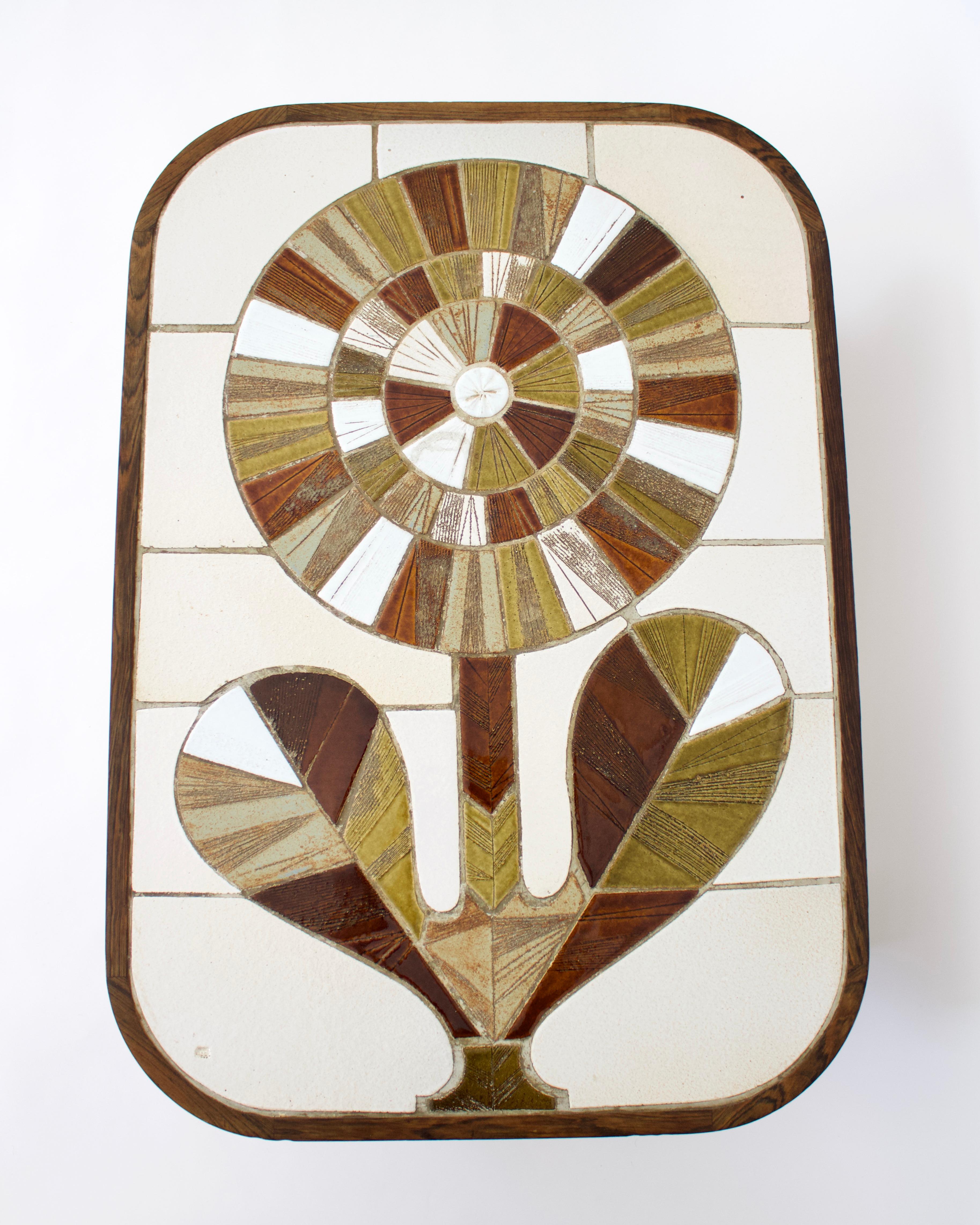 Table basse en céramique française de Roger Capron avec un vibrant motif de tournesol rayonnant. 
Couleurs vert olive et nuances de vert olive et de brun, de tan, de beige et de blanc. 
Tous les joints sont en place. Le cadre en bois est teinté en