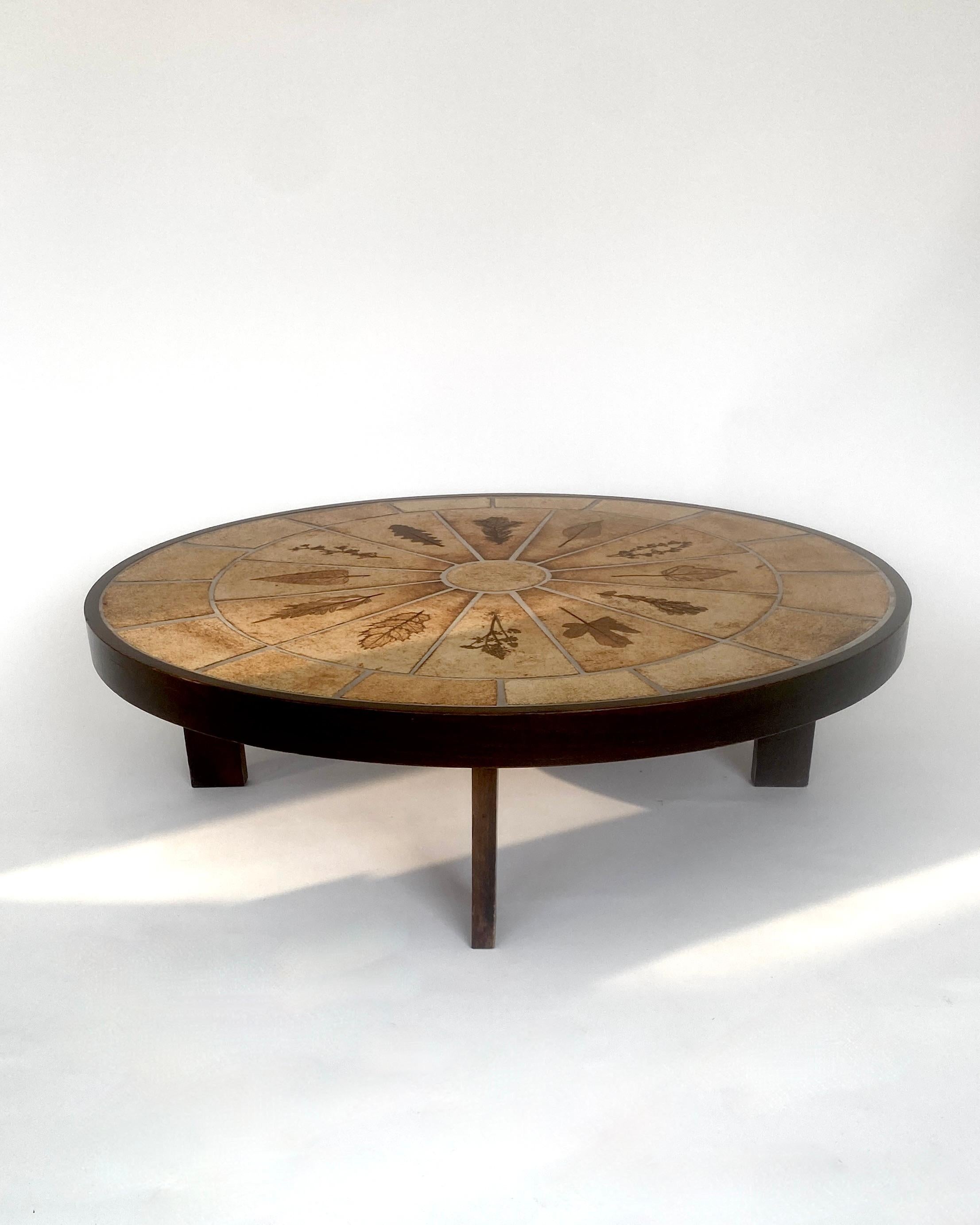 Tavolino in ceramica di Roger Capron con decorazioni a foglie impresse. Le foglie provengono dai boschi e dai giardini circostanti di Vallauris, dove Capron aveva il suo studio. 
Il tavolo è più ovale che completamente rotondo. Le piastrelle in gres