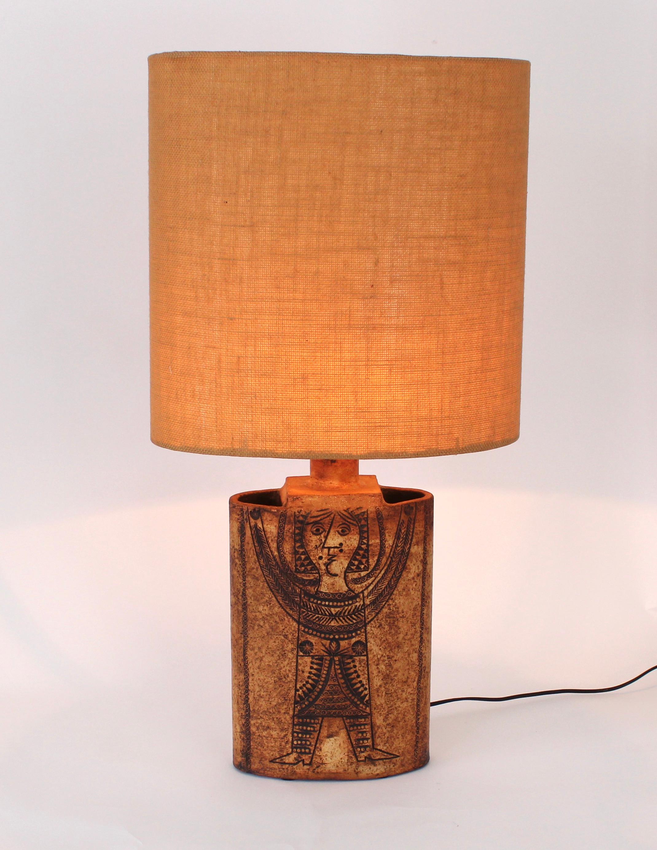 Roger Capron French figural ceramic table lamp. Original oval burlap shade. 
The clay gres is rubbed with iron oxides which penetrate into the incised drawing. 
The lamp is unglazed thus in the firing the iron oxides in the incised drawing burn to
