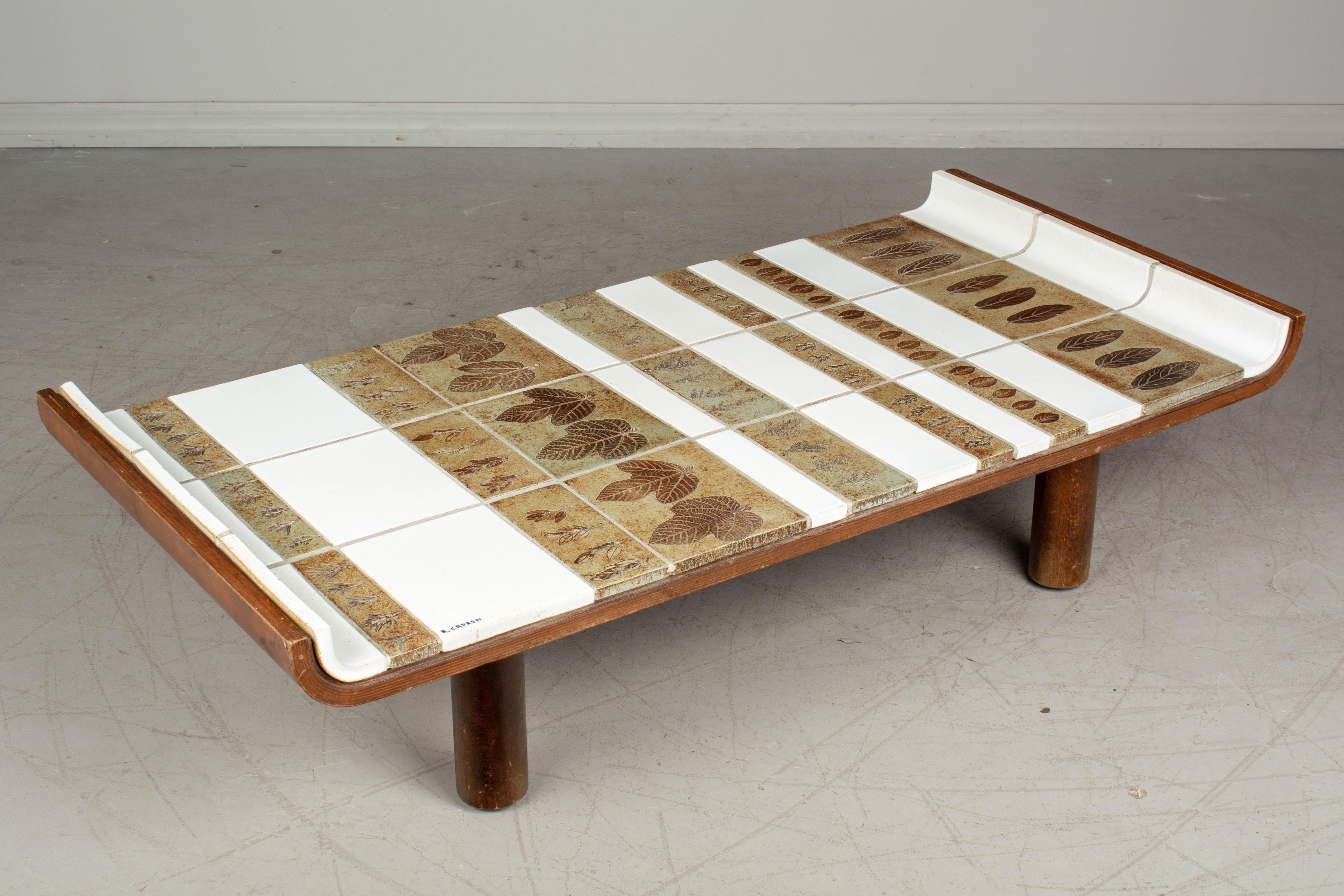 A French Mid-Century Modern Roger Capron pagode model ceramic tile coffee table. Oak frame with upturned edges and solid pillar legs. White glazed tiles and brown and greenish tone ceramic tiles with impressed leaves. Signed R. Capron. Small loss to