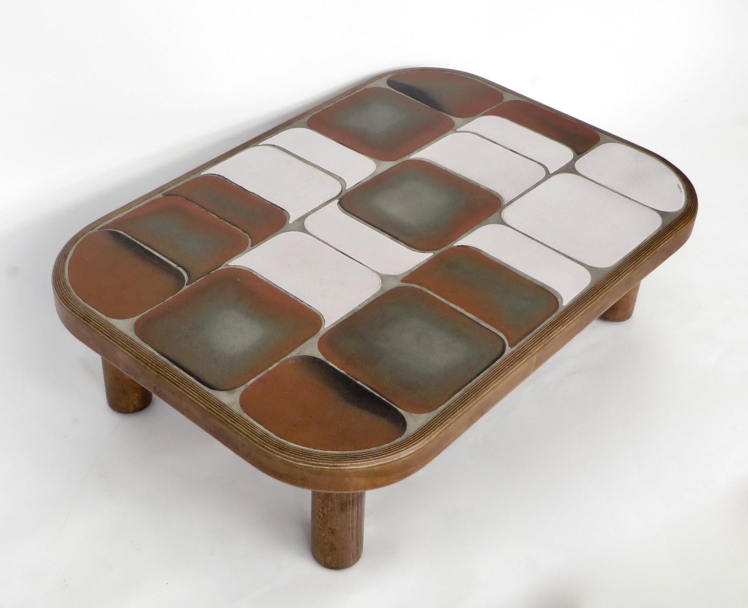 Table basse modèle Roger Capron Sho-Gun ou Shogun avec plateau en carreaux de céramique de couleur beige brun avec de légères nuances de vert et des carreaux blancs et émaillés sur base et pieds en acajou. Les couleurs varient d'une table à l'autre