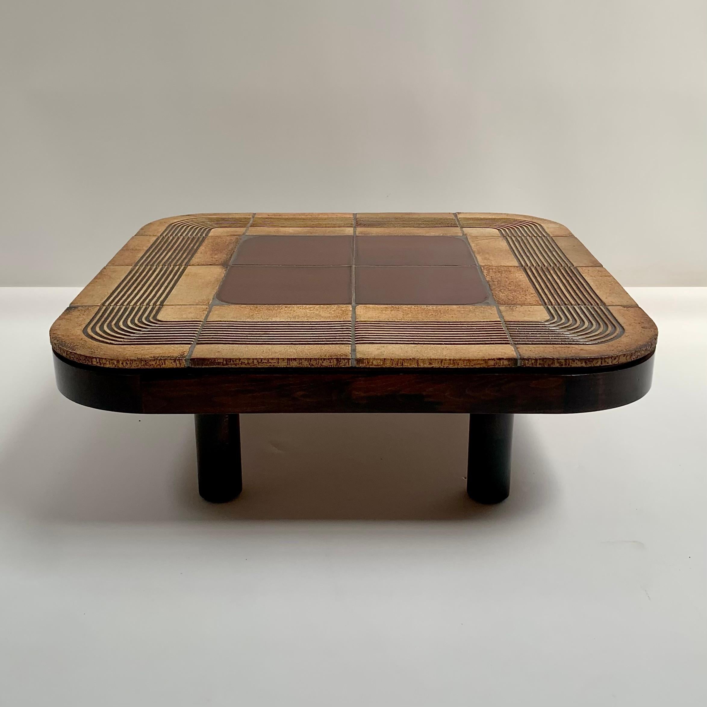 Schöner Couchtisch Modell Mambo, signiert von Roger Capron, CIRCA 1970, Frankreich.
4 zylindrische Füße aus brauner Eiche, braunem Sperrholz und emailliert  beige, braune und schwarze Keramikfliesen. 
Signiert Capron auf der Oberseite.
Dieses