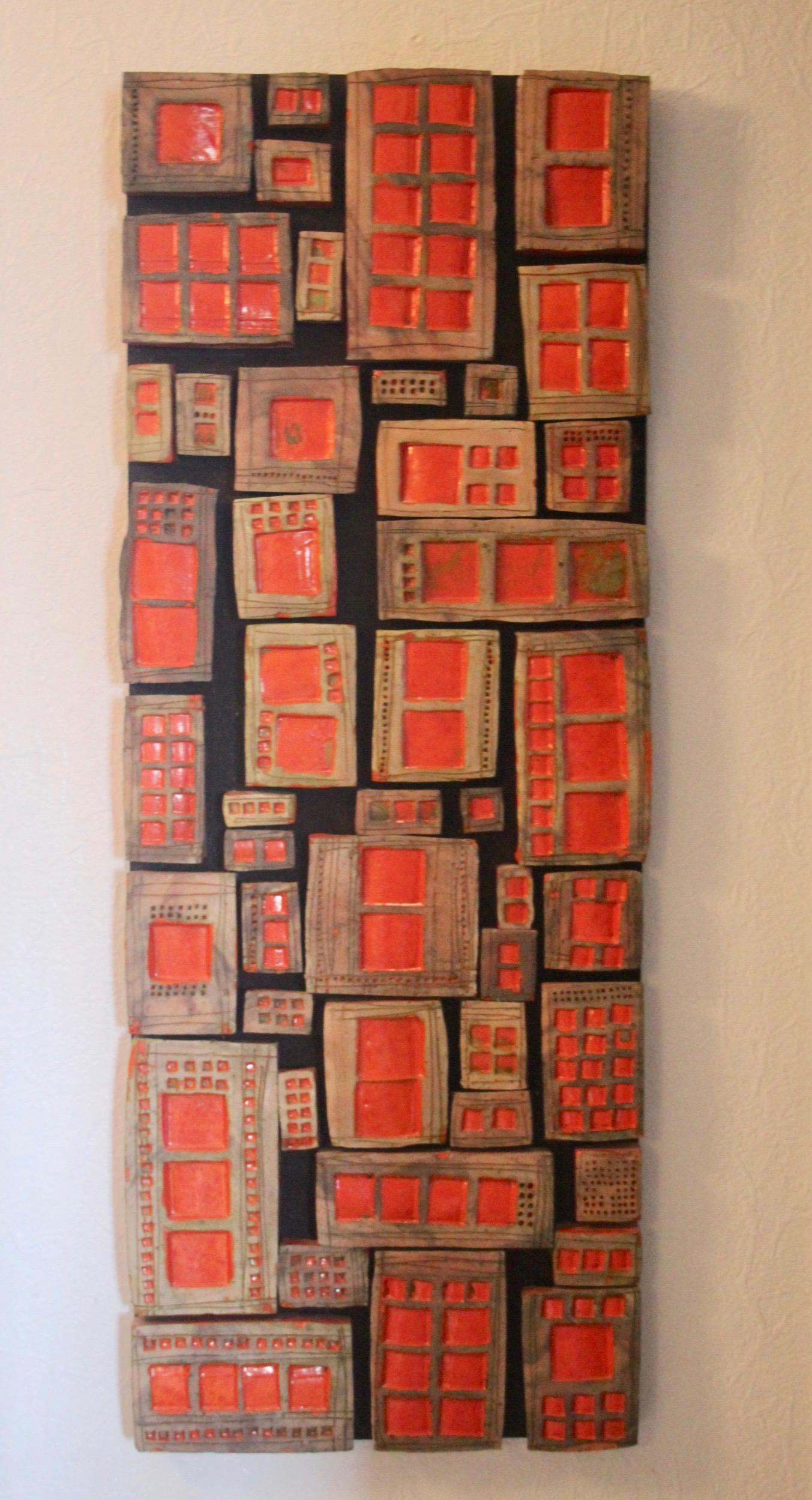 An assembly of individual ceramic blocks glued to a wood panel, representing a building or a block of houses. Similar to the work of French ceramist Roger Capron.