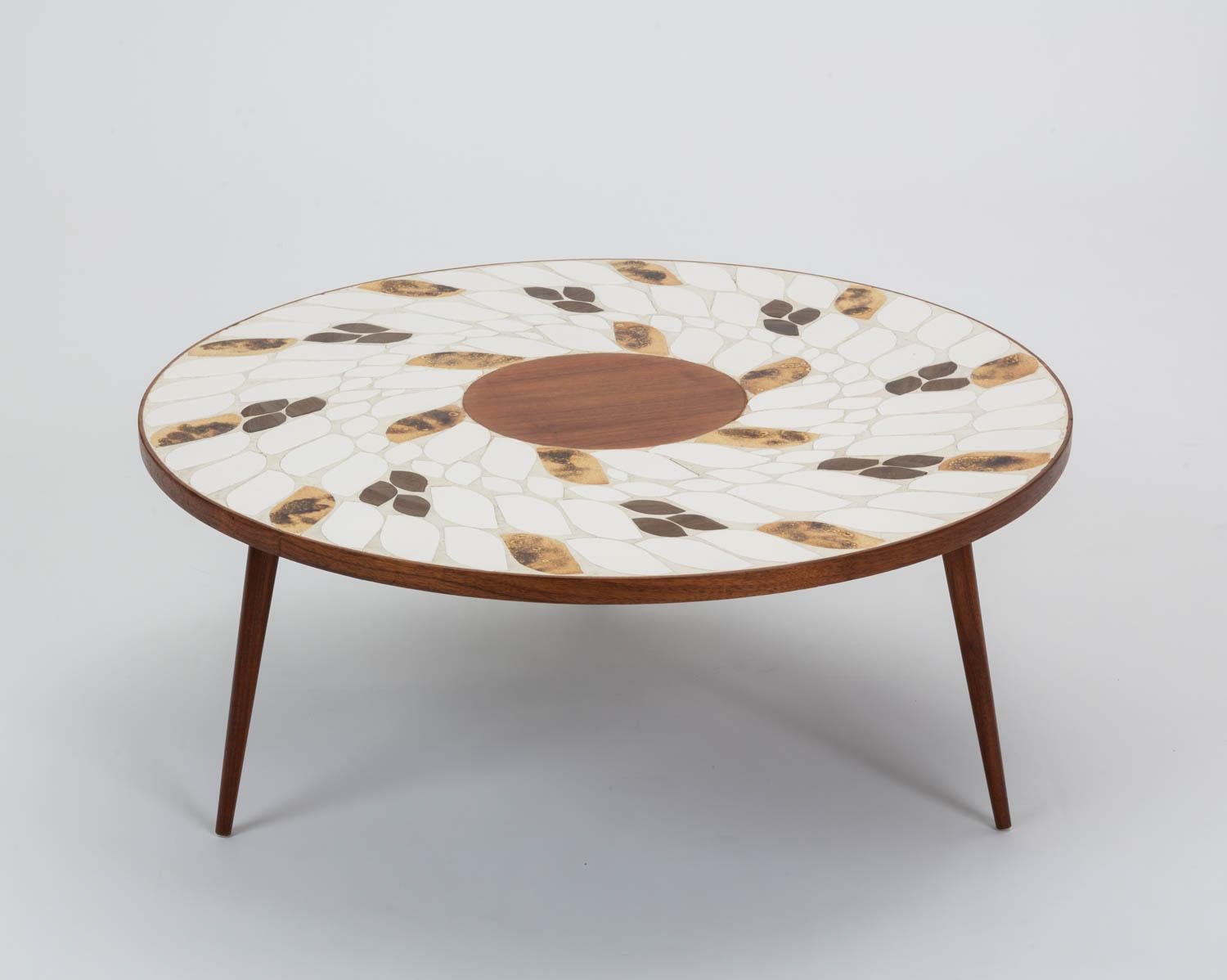 Ceramic tile coffee table in the style of Roger Capron, 1960s. The table features multicolored tiles in gold, light brown and bright white tones inset in to a round walnut frame that sits atop three tapering turned legs. 

Condition: Excellent