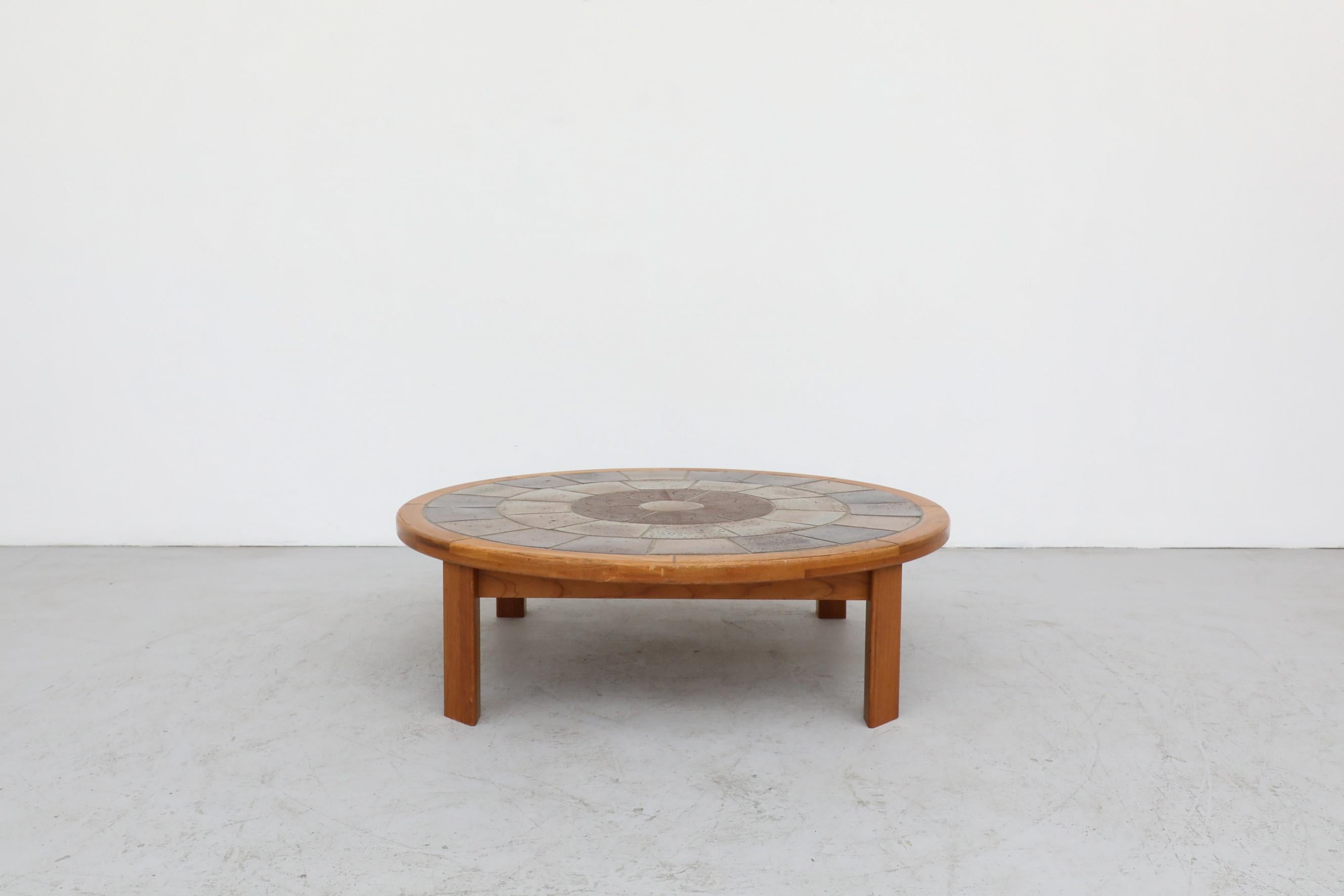 This Roger Capron style tile and oak coffee table by Tue Poulsen has imprinted ceramic tiles set in a dial design and a lightly refinished frame. It's in original condition with a few minor scratches and no structural damage. The wear is consistent