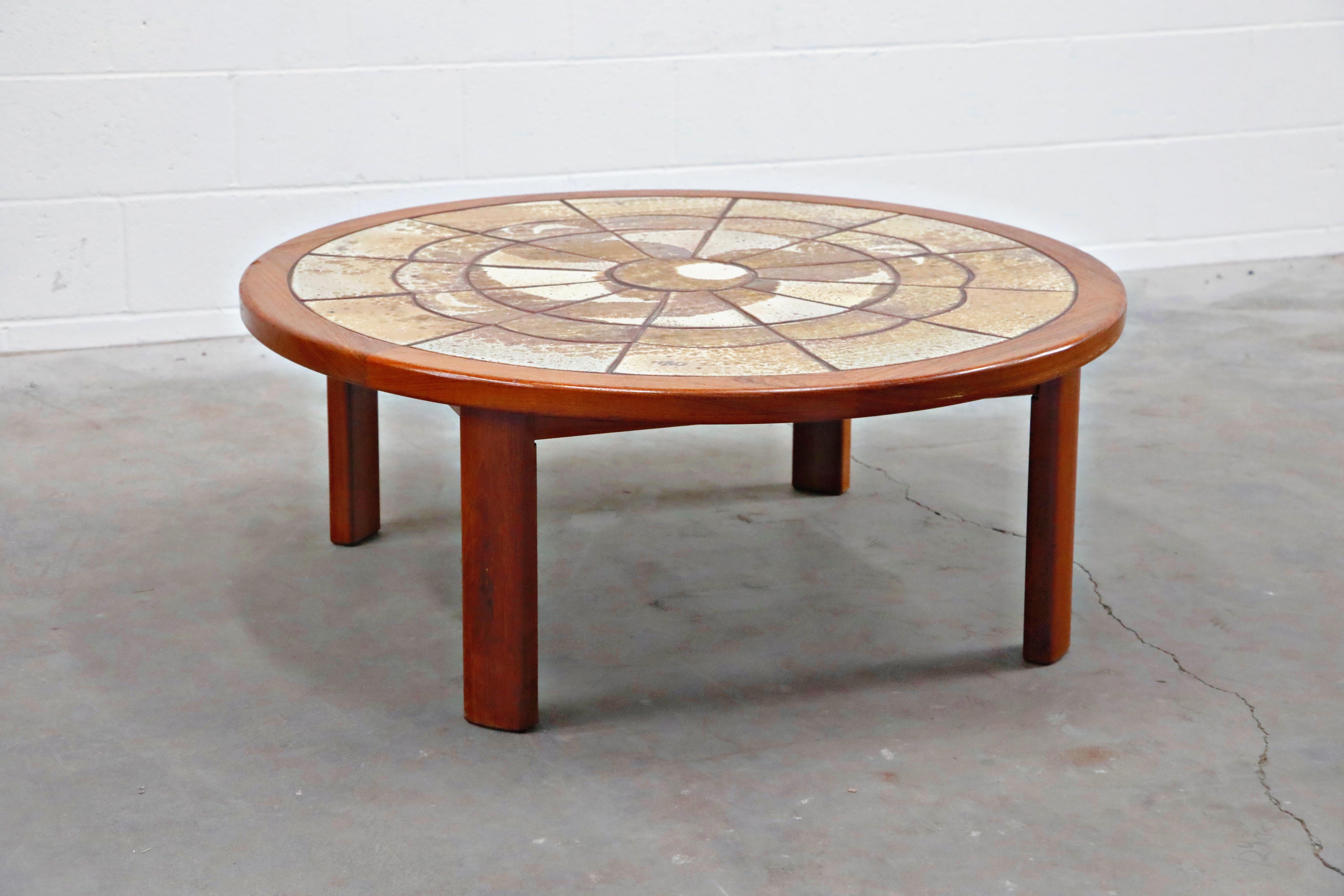 A classy and stylish Tue Poulsen and Roger Capron style Mid-Century Modern teak and ceramic tile coffee table featuring ceramic art tiles inset into a round teak top atop for teak legs. The ceramic tiles are placed in a circular pattern with a cloud