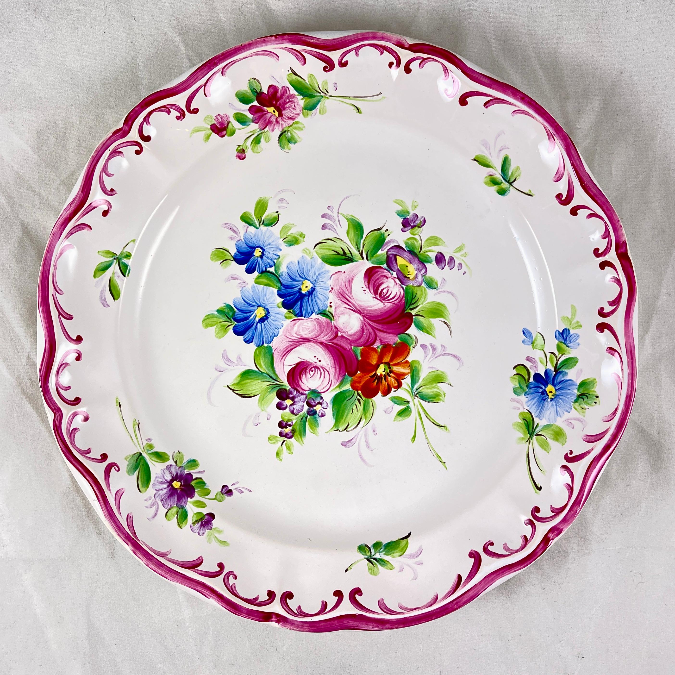 A hand painted floral plate made by Roger Colas, Clemecy Nievre, France, circa 1930s.

A tin-glazed white earthenware plate showing a shaped rim outlined in a bright pink glaze. A central floral bouquet of stylized light pink roses, blue daisies,