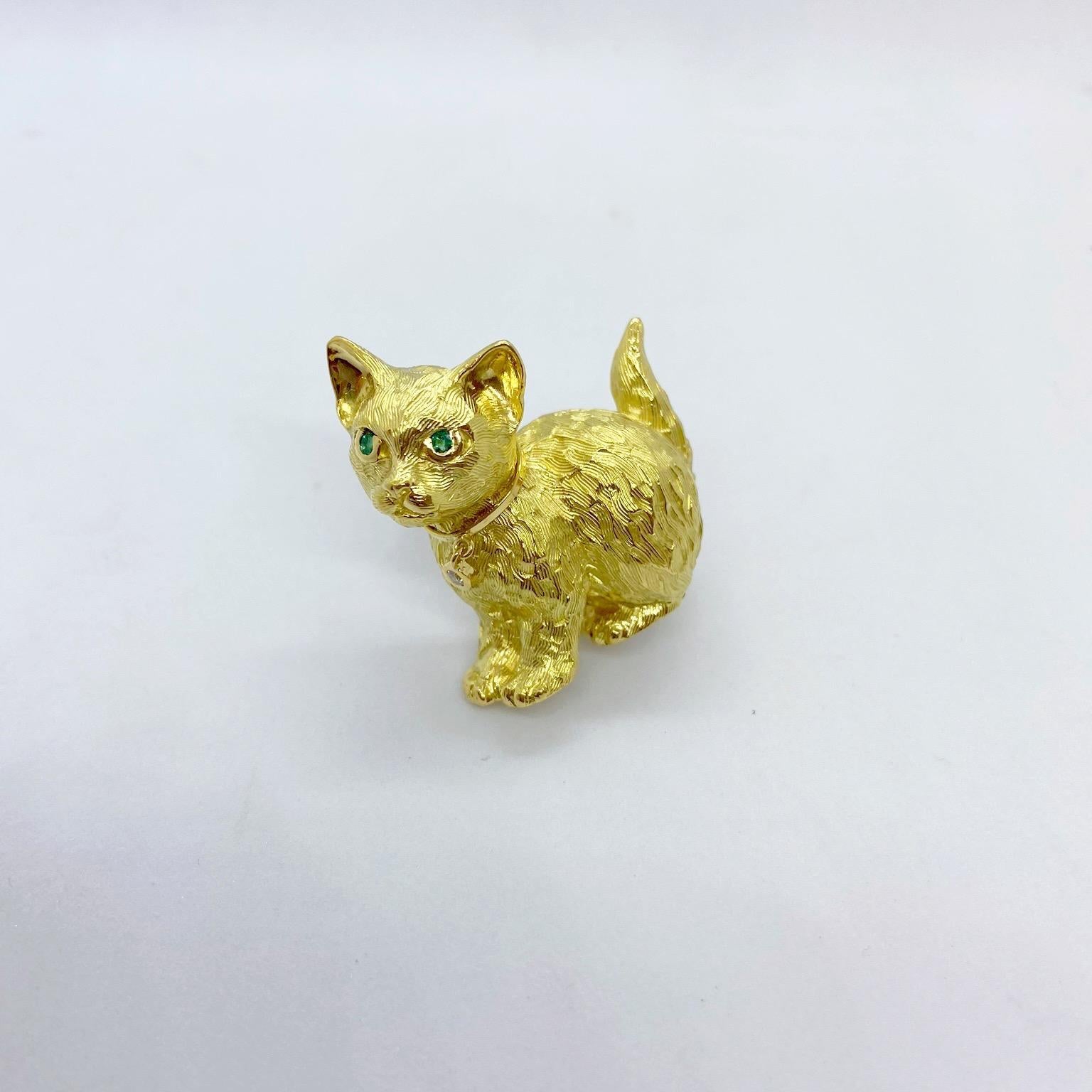 Crafted by Roger Guillochon ,from France for Cellini Jewelers, this 18 karat yellow gold cat brooch depicts magnificent craftsmanship. The cat's body is etched in a satin/hi polish finish. His eyes are set with emeralds and from his collar dangles a