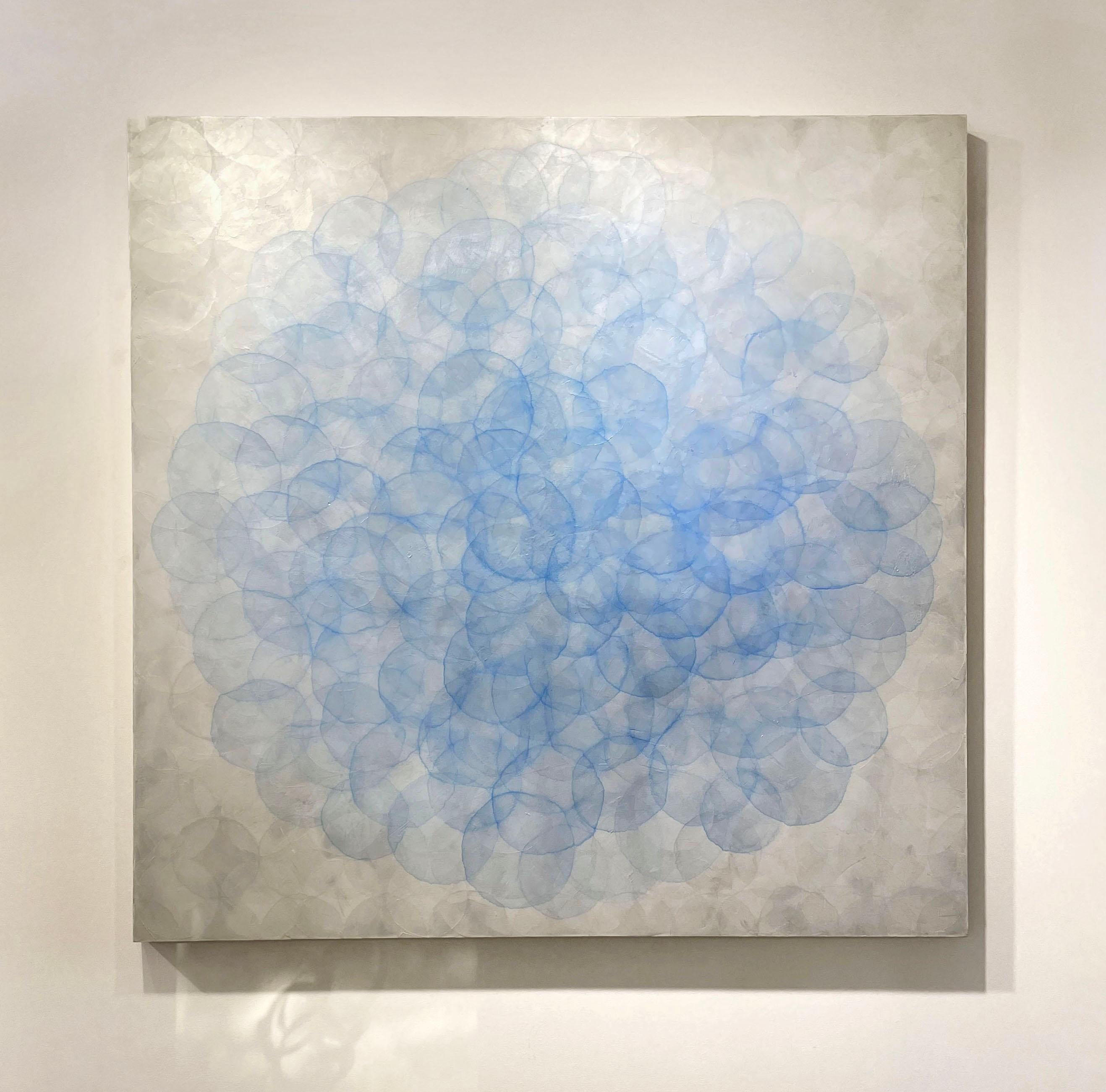 This large abstract contemporary statement painting by Roger Mudre features many light circle shapes, layered over one another in a concentric fashion and a cool blue and silver palette. The piece is made with acrylic paint over marble dust and mica