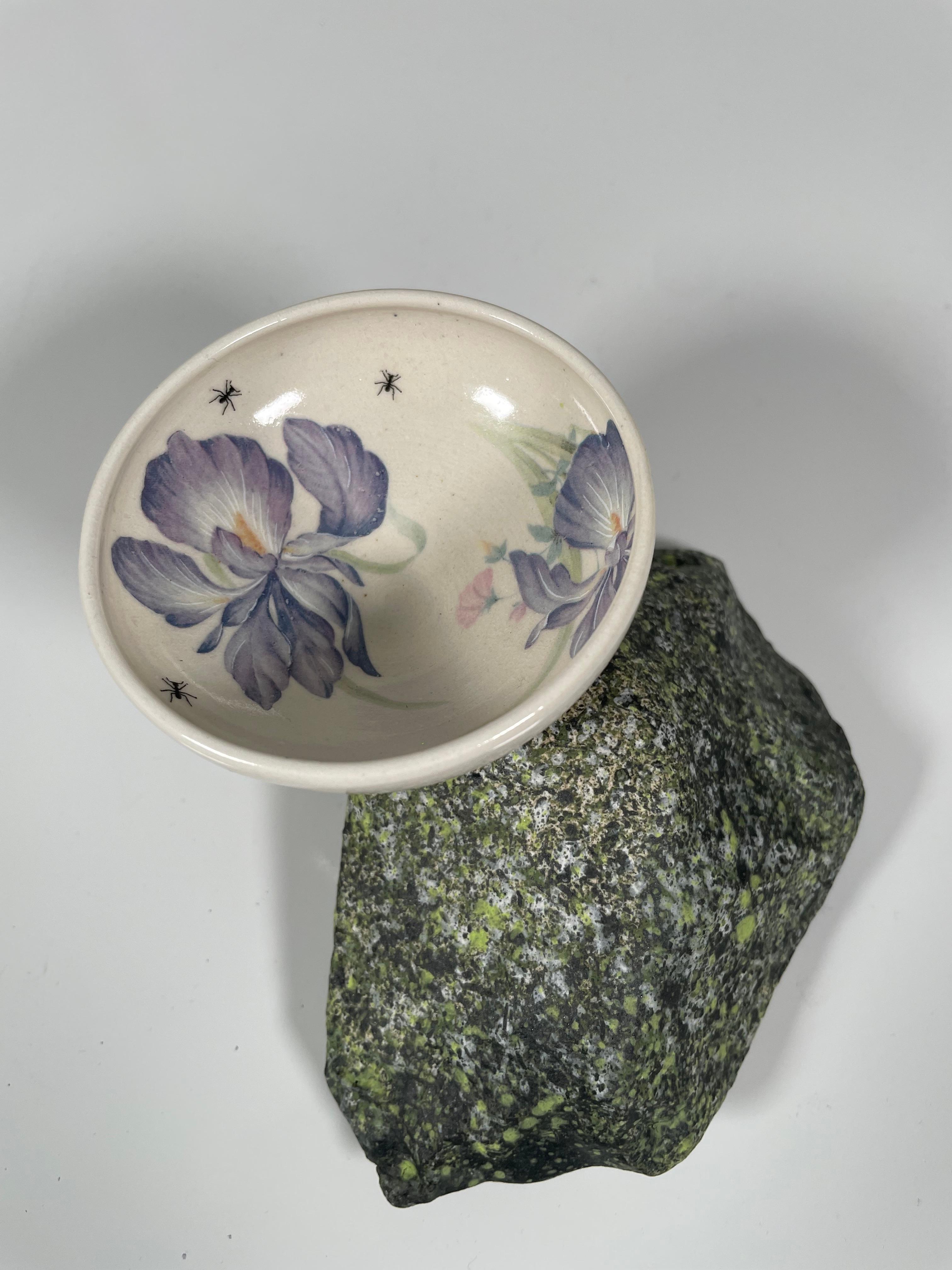 This 3" x 6 " x 5" ceramic work by Oklahoma artist, Roger Runge consists of a wheel-thrown porcelain bowl positioned on a handmade porcelain base sculpted to resemble a natural rock formation. The surface decoration employs commercial ceramic decals