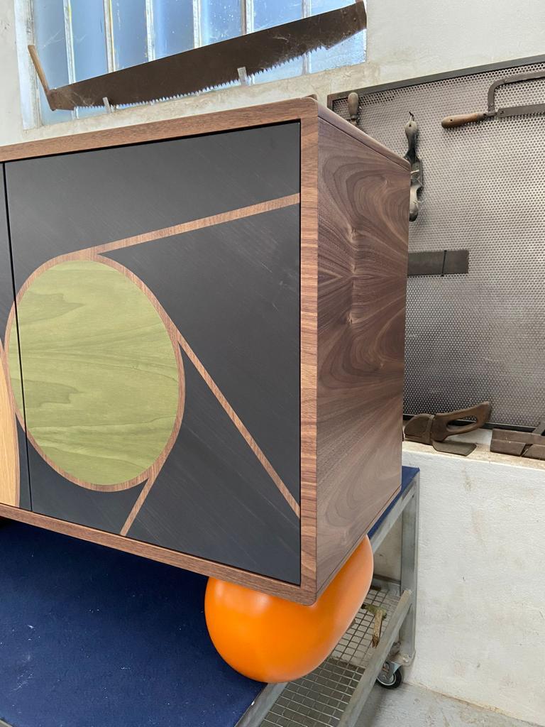 This Orange legs side cabinet is a revised version of our famous Roger cabinet. 
It comes with a round edges walnut veneered carcass and 4 doors colourfully veneered with a circle pattern that continues on the border of the doors to create the