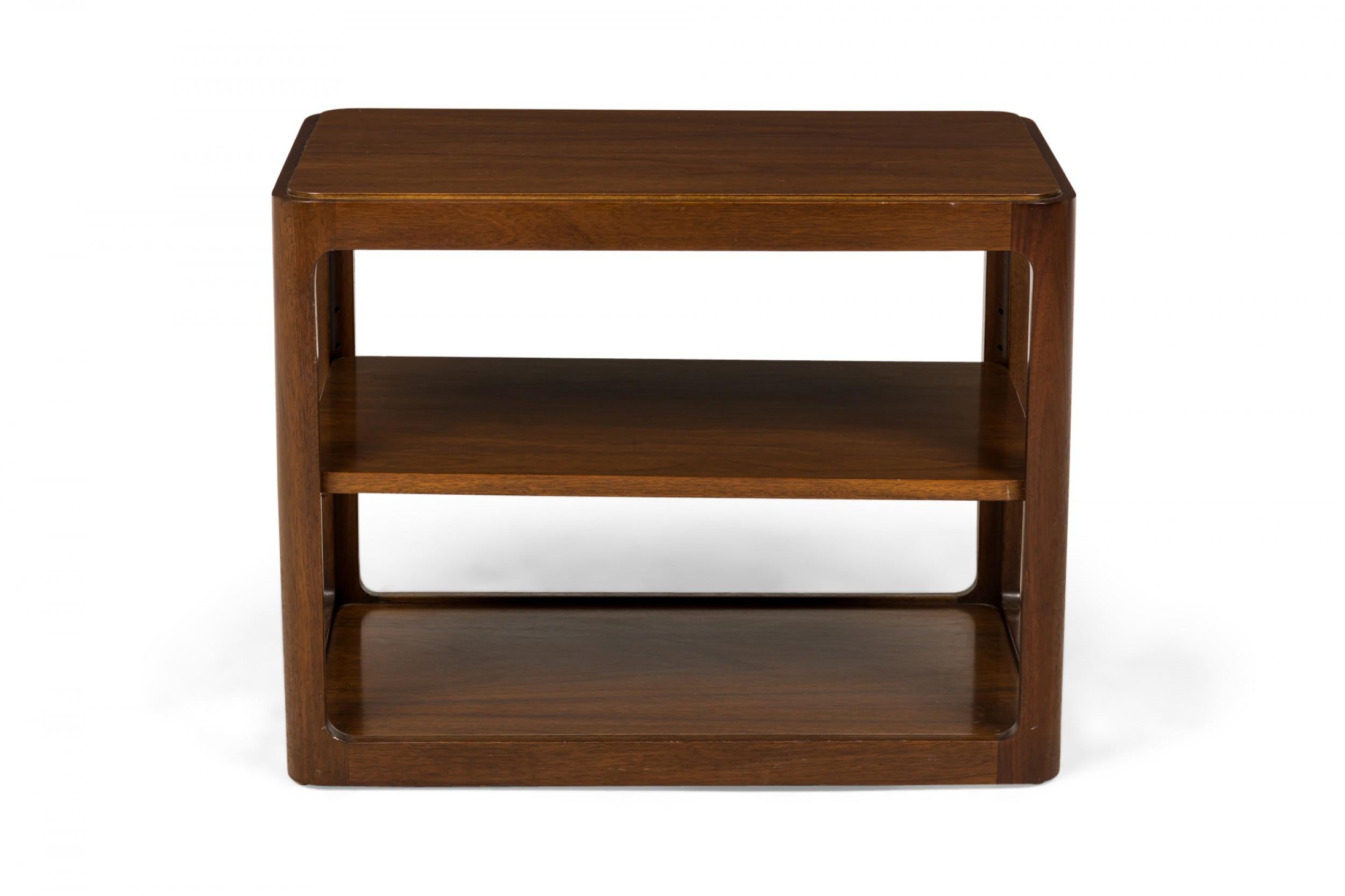 American Mid-Century 'Radius' form rectangular end / side table with a wooden frame, a slightly lighter raised wooden tabletop with rounded edges, and a middle stretcher shelf, resting on a solid base that creates and additional lower open