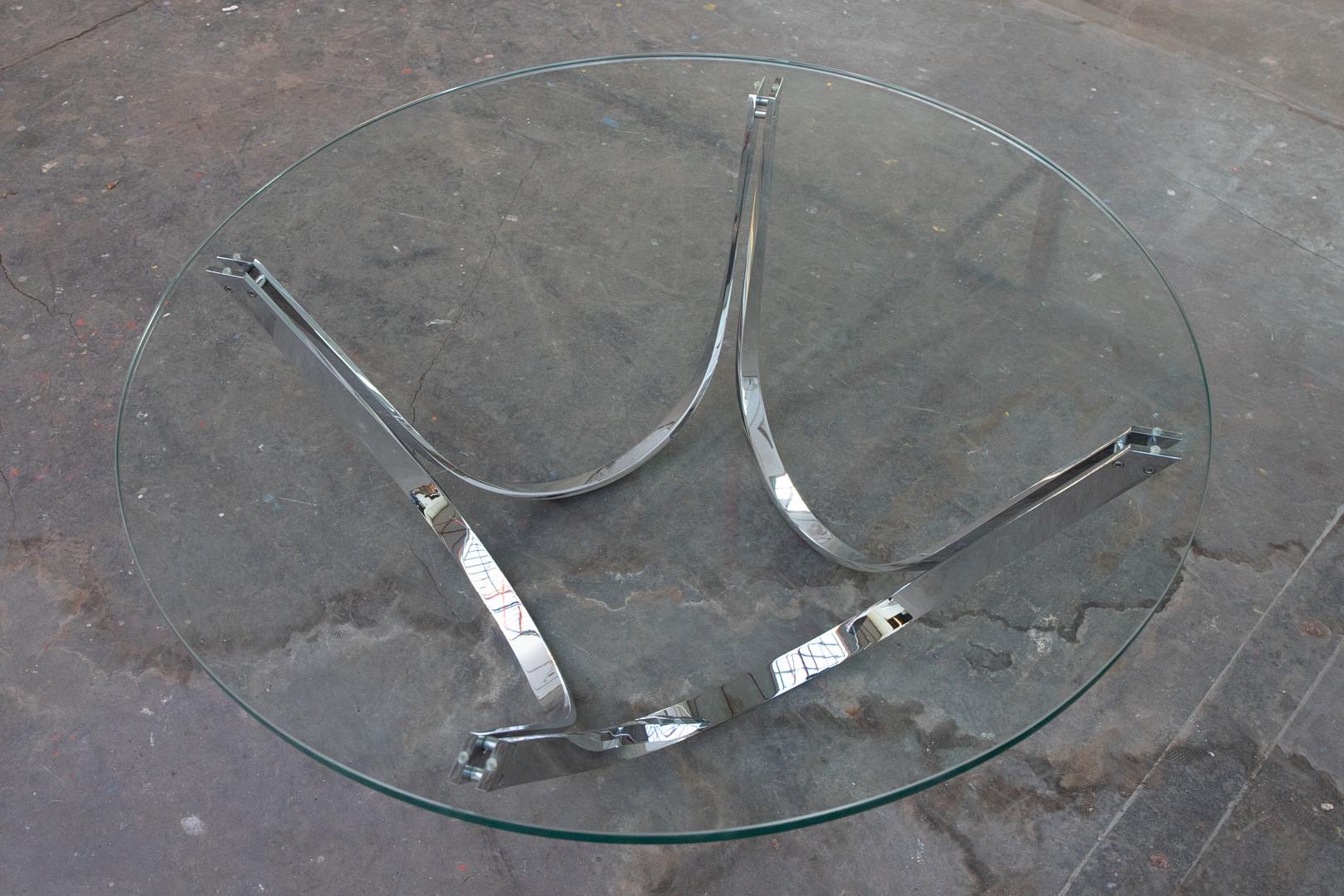 Table basse ronde contemporaine conçue par Tri-Mark. La base, en nickel, se présente sous la forme de quatre éléments en forme de U renversé supportant un plateau rond.  Prix supplémentaire pour le plateau en verre. 