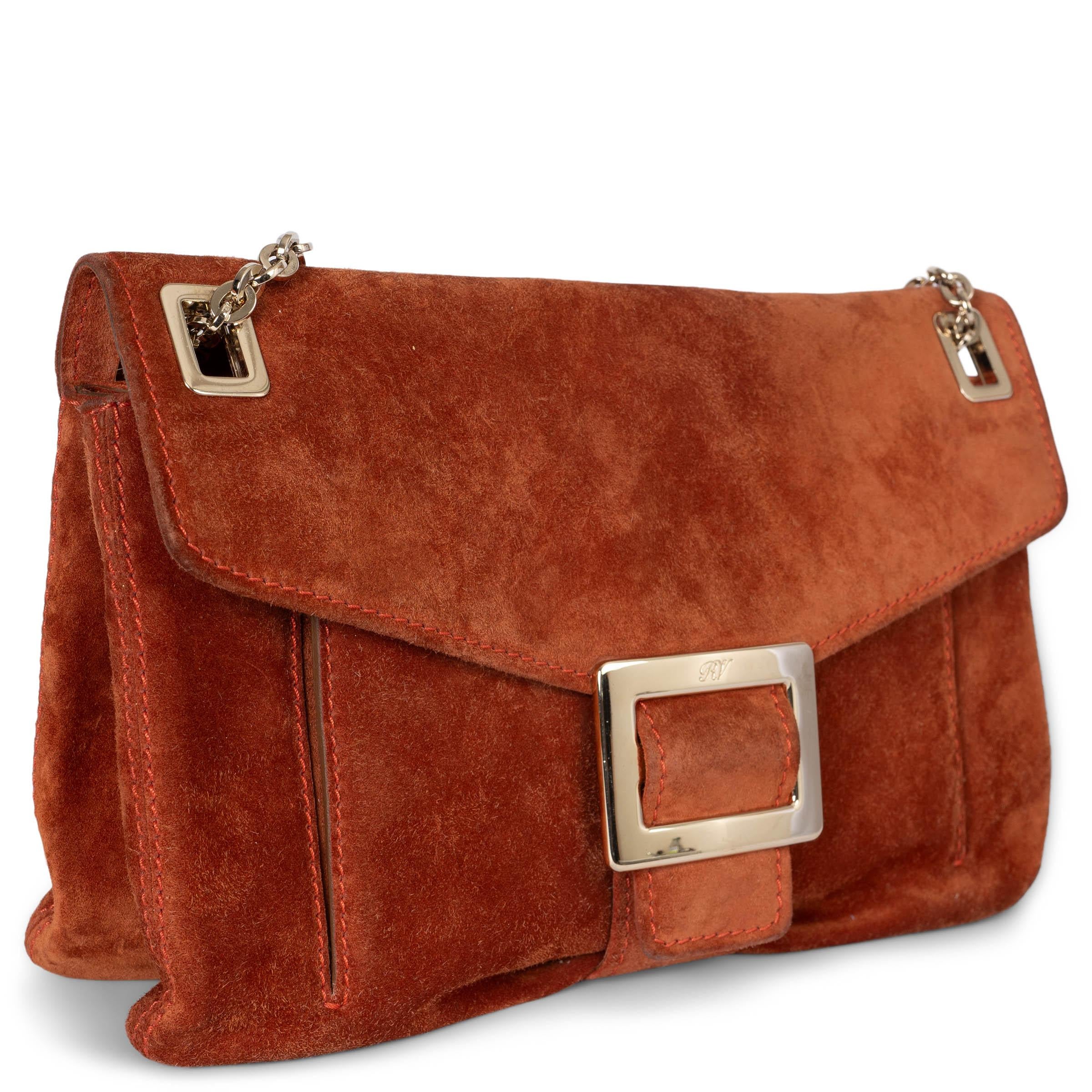 This 100% authentic Roger Vivier Metro Medium flap shoulder bag in rich brick suede combines elegance with functionality. It features light gold-tone hardware and a versatile chain strap, allowing it to be worn over the shoulder or crossbody. The