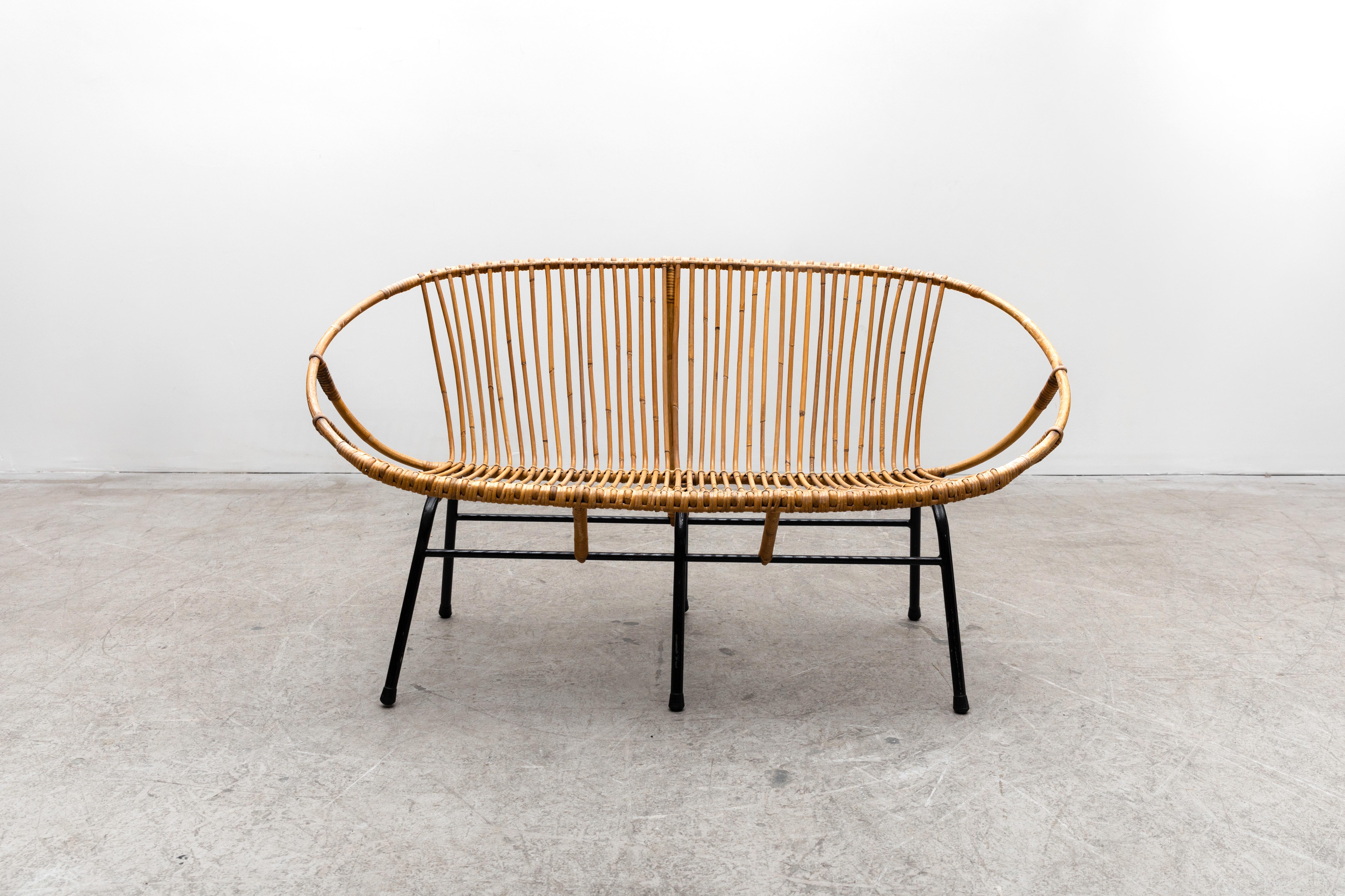 Rohé Noordwolde bamboo loveseat with black enameled tubular base. In original condition with visible patina. Minimal rattan loss and breakage. Frame shows wear and scratching. Wear is consistent with it's age and use.