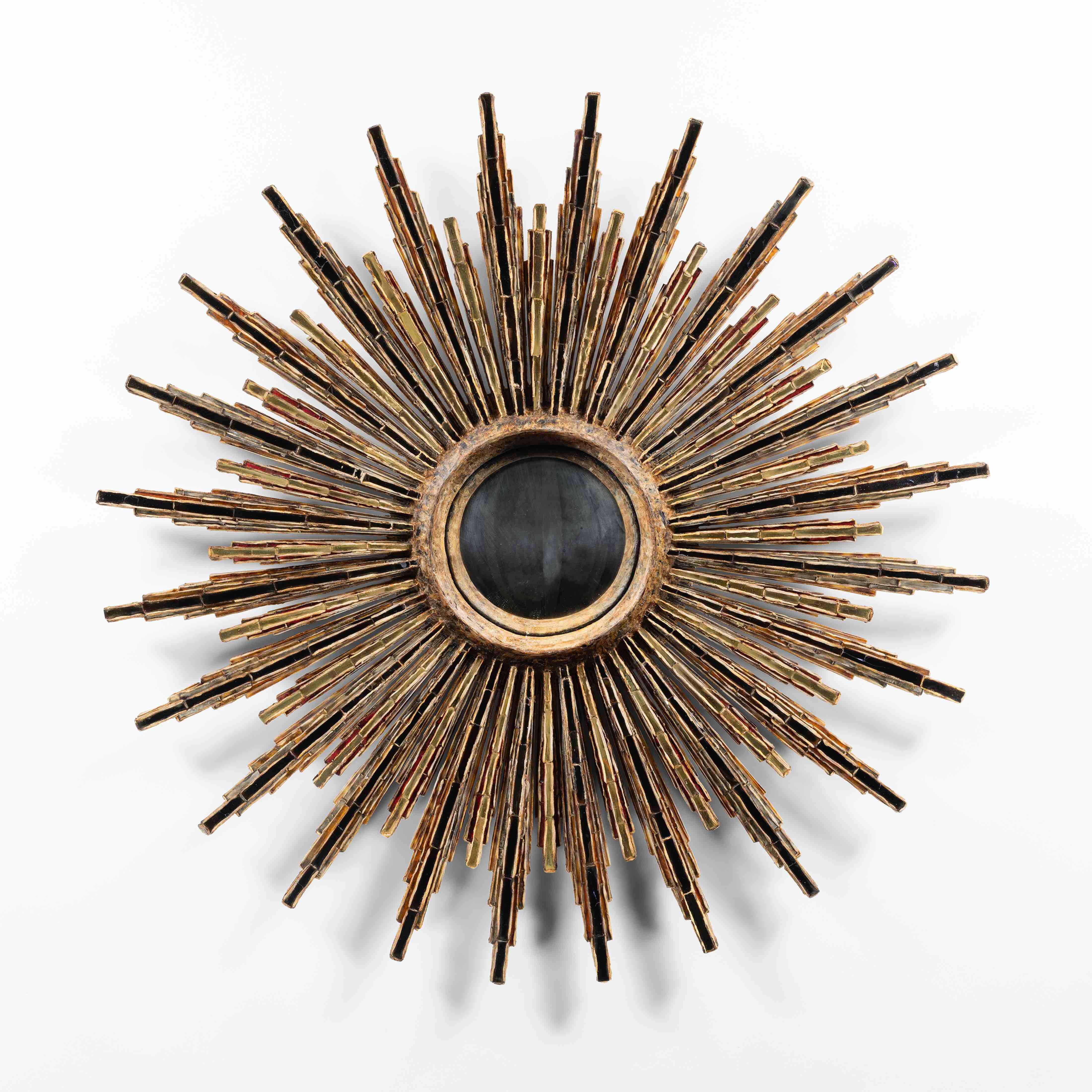“Roi Soleil” by Line Vautrin – Talosel mirror
Light brown talosel structure whose rays (24 large rays, 24 small) are encrusted with alternating bronze, gold and red mirrors.
A thick circle of talosel surrounding the witch central mirror. The edges