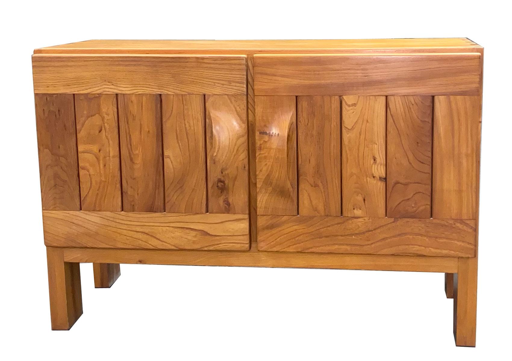 Regain - circa 1960 Roland Hauesler 
Commode en orme à cadre rectangulaire ouvrant par deux portes à panneaux et poignées sculptées, équipée d'un tiroir et d'une tablette formant étagère et reposant sur quatre pieds poutre à réception plate.
De