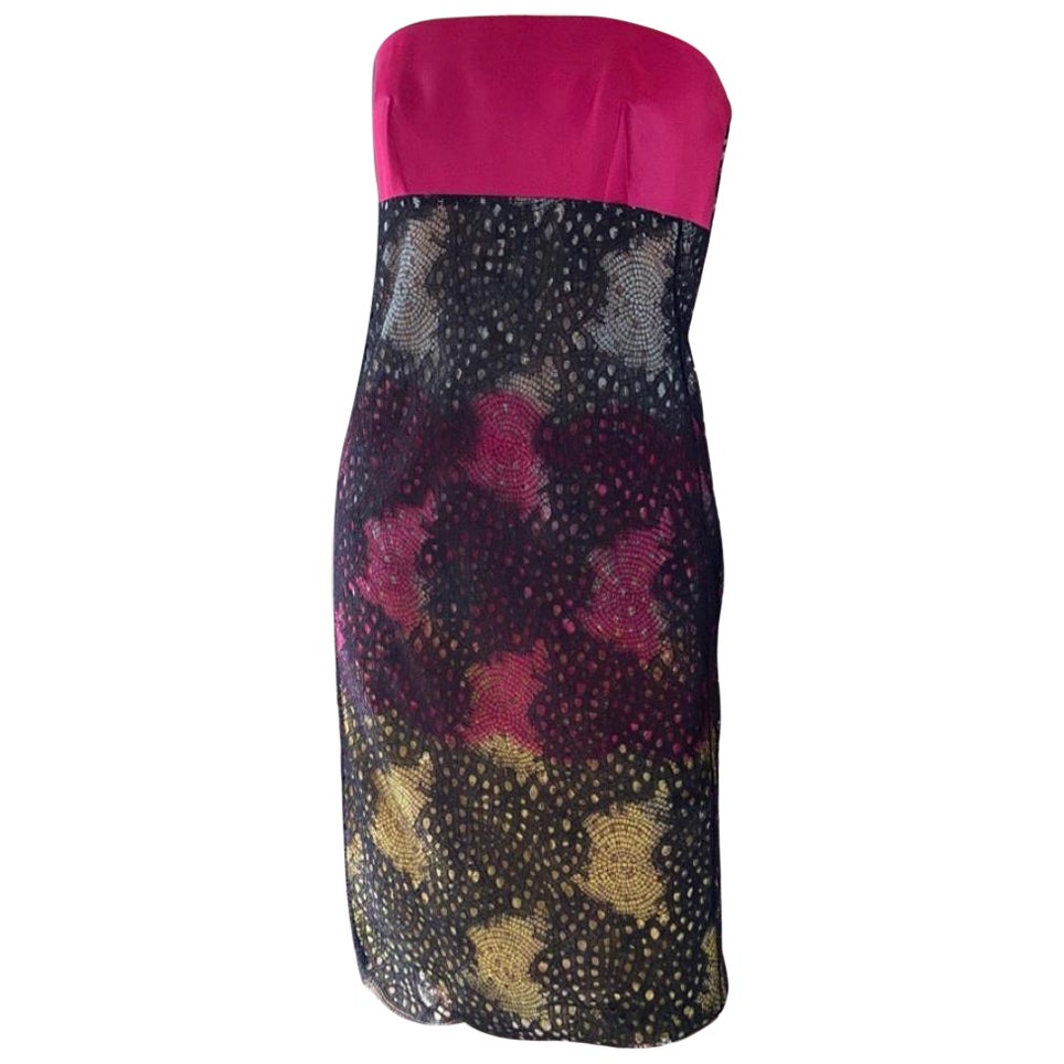 Una maravilla del diseñador francés Roland Mouret.  Vestido sin tirantes de encaje y satén, el busto es de satén lacado y el encaje tiene un intrincado estampado multicolor. El escote está reforzado y la moderna cremallera de latón prolonga la