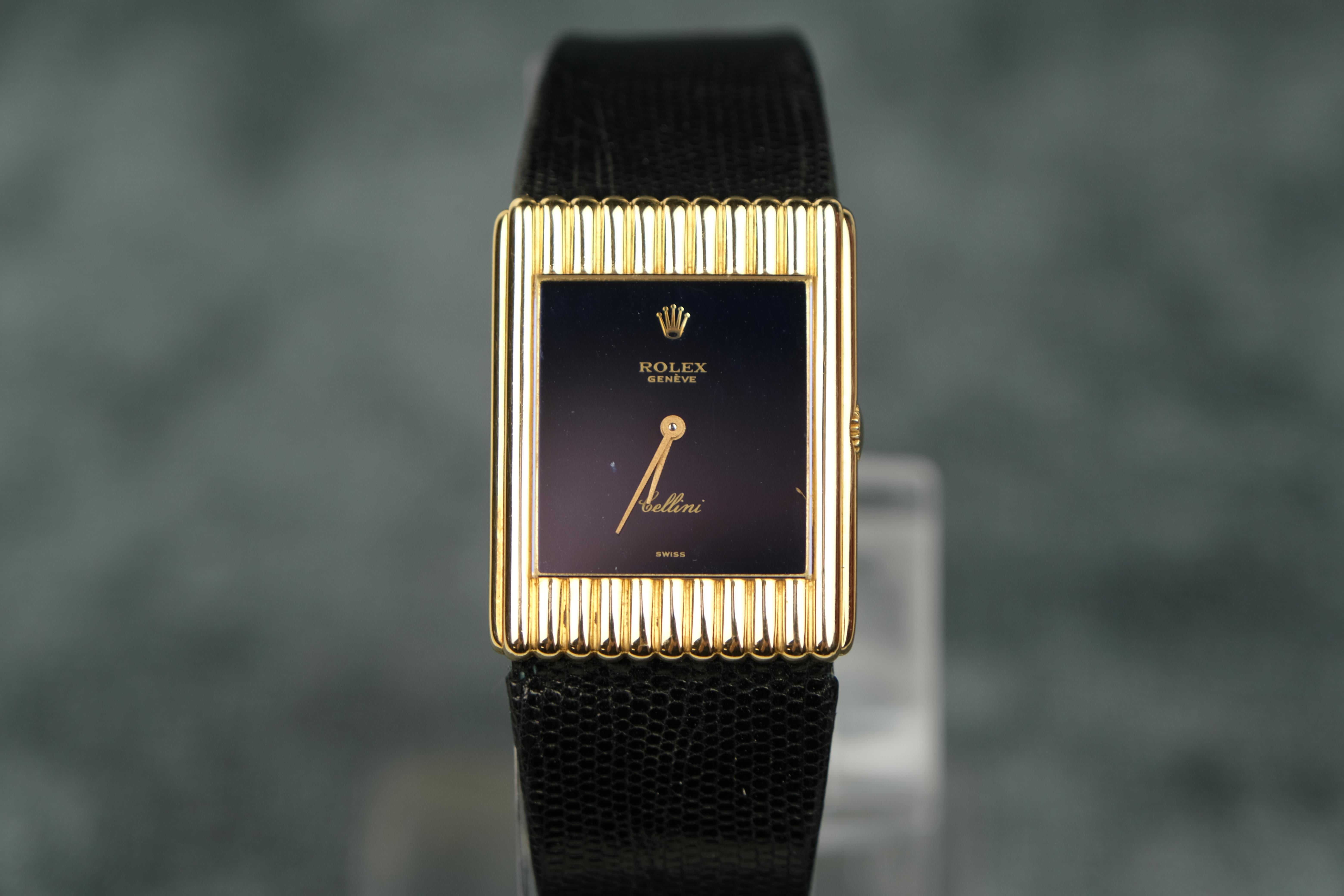 Rolex Cellini 18K Gold Stem Wind Wristwatch

A luxury timepiece with a tank-style 18K yellow gold bezel that frames a navy blue dial with Rolex hallmark crown and gold-tone baton-style hands.

This elegant watch also features an 18K yellow gold case
