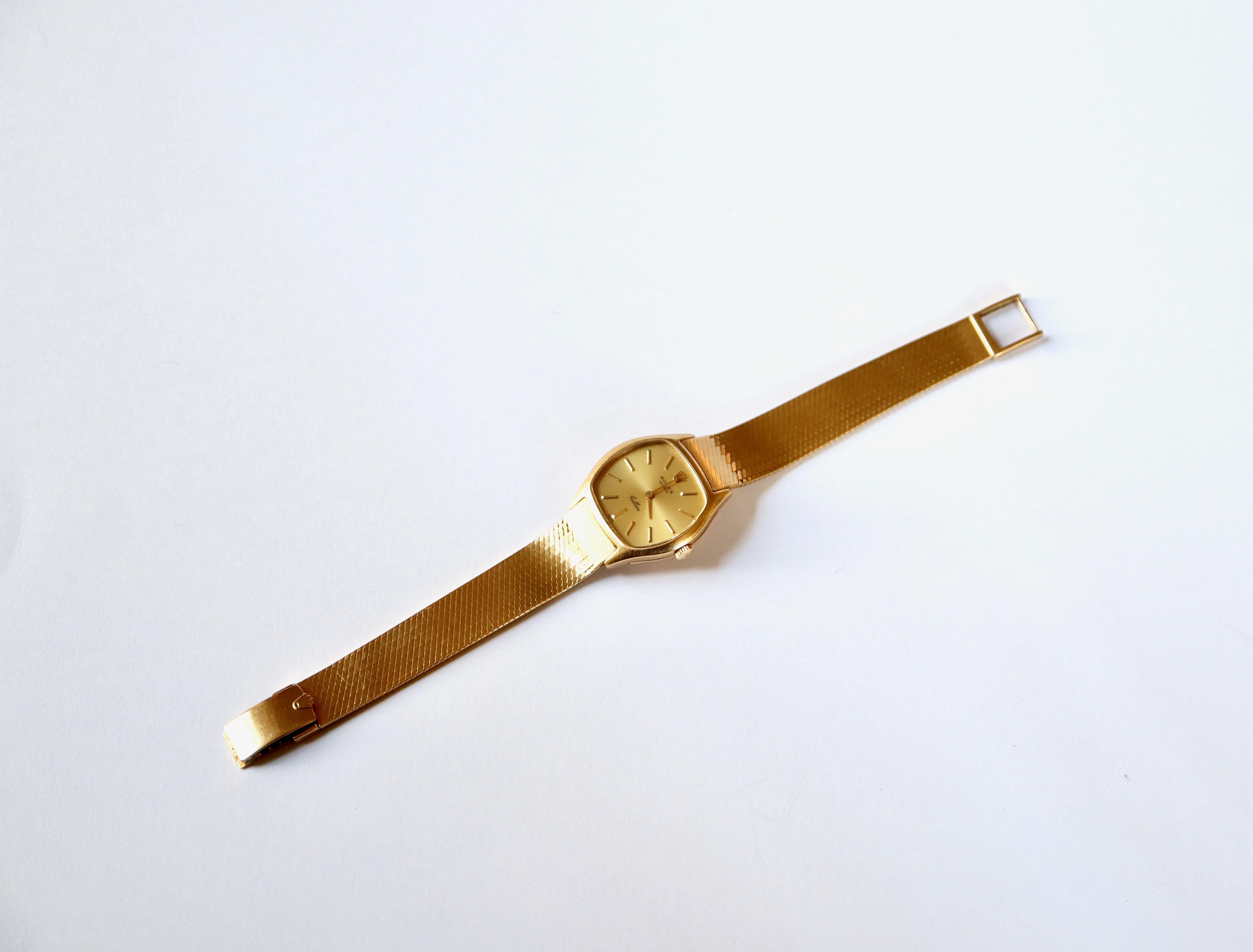 Rolex lady's wristwatch in 18K yellow gold, Cellini model, curved rectangular dial with gilt background, applied baton indexes. Mechanical movement. Gold crown. Flexible bracelet in 18 kt gold, invisible mesh with safety clasp, adjustable position.