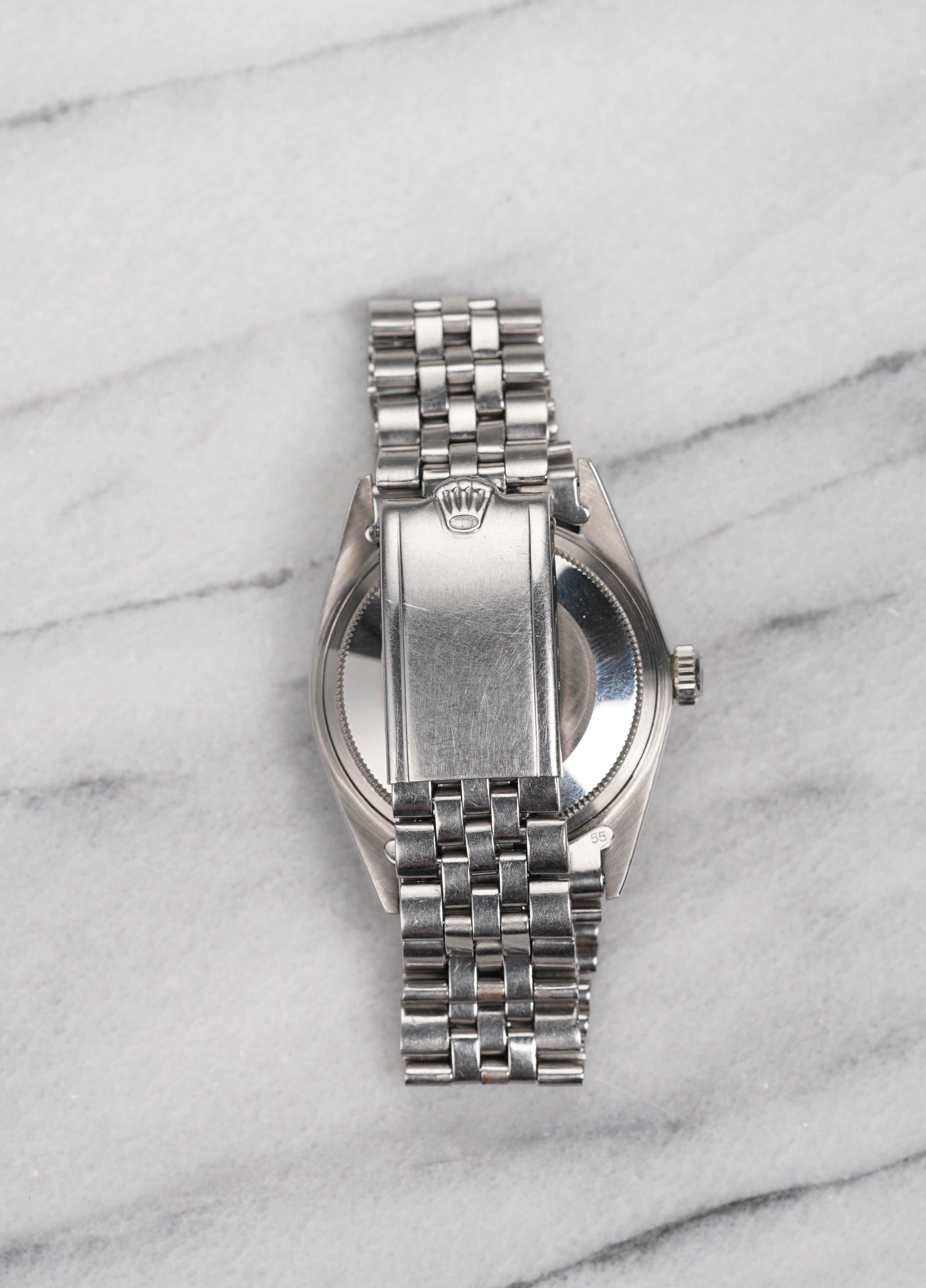 Aquí tienes un Rolex Datejust vintage de referencia 1603 automático con una esfera lavanda/tapo sunburst (la esfera adquirió un tono violáceo a partir de su esfera plateada original) en un brazalete jubilee de los años 70. Mantiene la hora y es