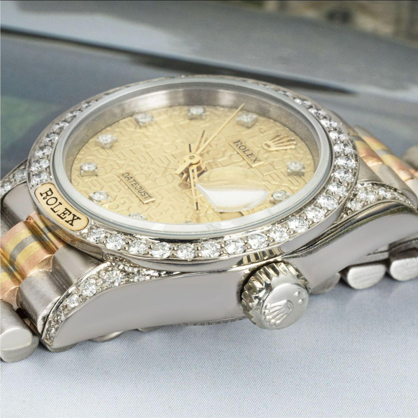 A 26mm ladies Datejust in tri-gold by Rolex. Featuring a champagne dial with diamond set hour markers and a fixed white gold bezel set with 36 round brilliant cut diamonds as well as 24 brilliant cut diamond set lugs.

Fitted with a sapphire glass,
