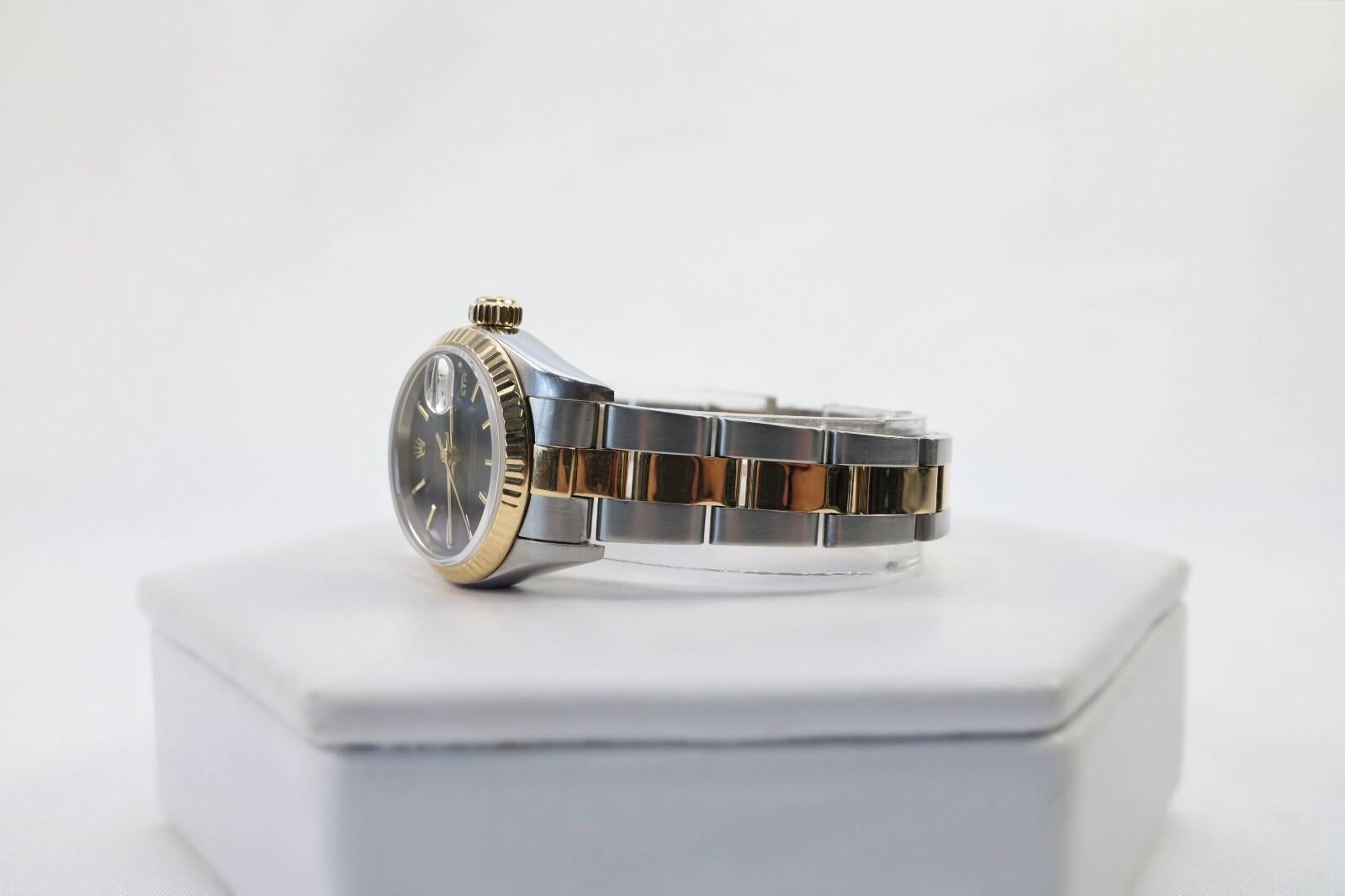 Este Rolex Datejust Ref. 79173 es un intemporal reloj automático de señora de 26 mm, fabricado en acero inoxidable y oro amarillo de 18 quilates. Presenta una esfera azul oscuro con índices dorados, una lupa Cyclops sobre la ventana de la fecha y un