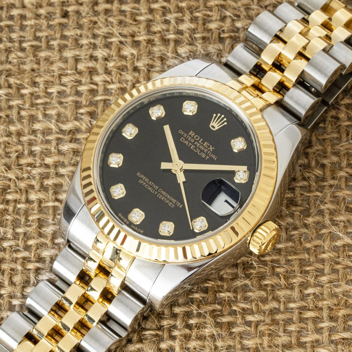 A 31mm mid-size Datejust in Oystersteel and yellow gold by Rolex. Features a black dial with diamond set hour markers and a fluted yellow gold bezel.

Fitted with scratch-resistant sapphire crystal and a self-winding automatic movement. The watch is