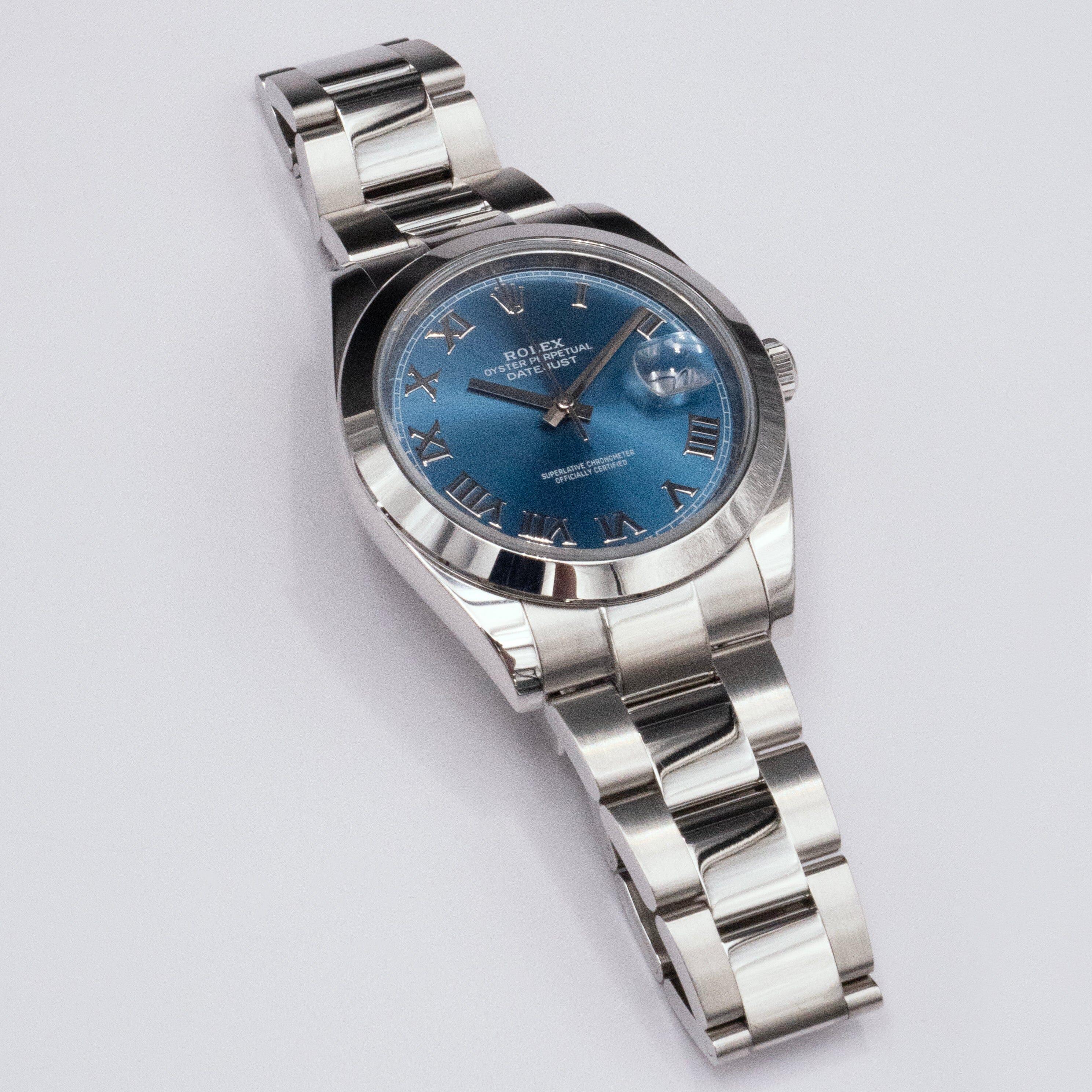 Rolex Datejust 41 126300 Orologio da uomo. Cassa in acciaio inossidabile da 41 mm. Lunetta levigata in acciaio inossidabile. Quadrante blu con lancette in acciaio e indici a numeri romani. Datario a ore 3. Bracciale Oyster in acciaio inossidabile