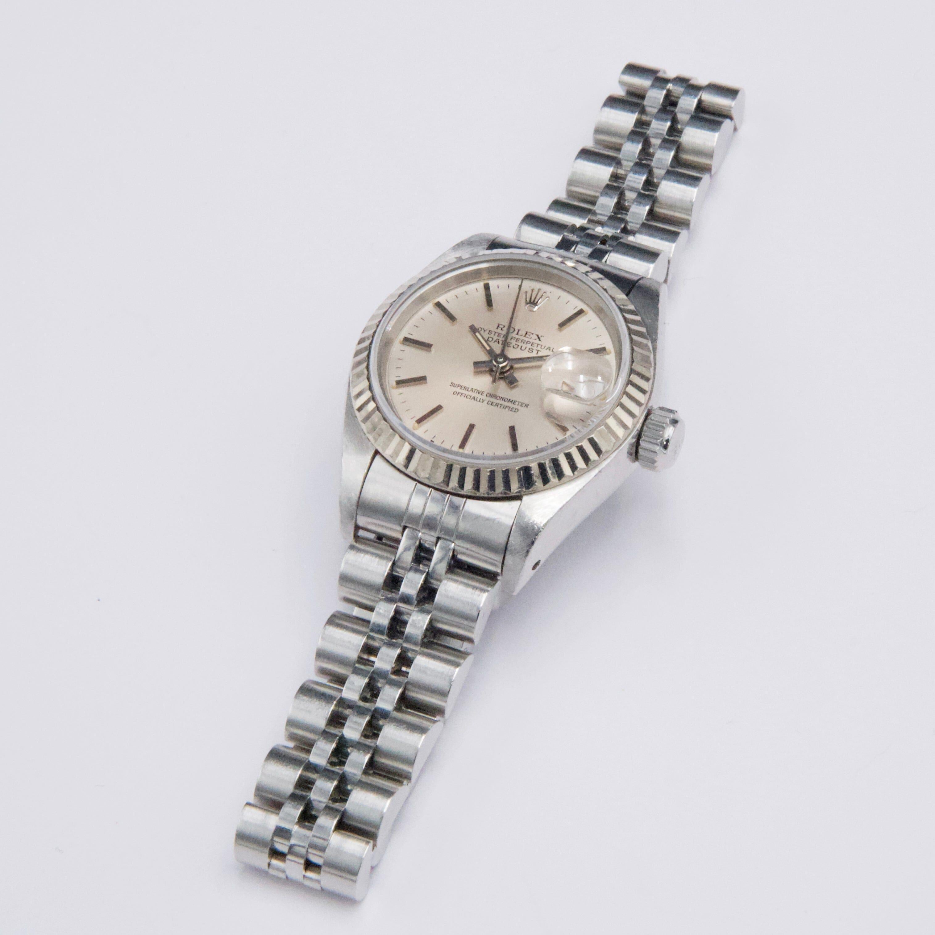 Rolex Datejust 69174 Ladies Watch. 26mm stainless steel case with 18K white gold fluted bezel. Silver dial with luminous steel hands and index hour markers. Minute markers on the outer dial. Date display at the 3 o'clock position. Stainless steel