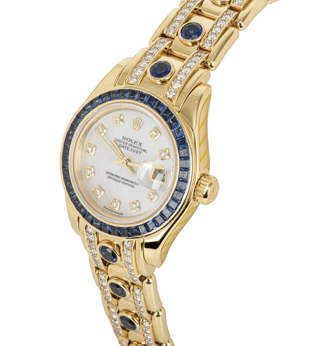 A Yellow Gold 29mm Datejust Pearlmaster by Rolex. Features a mother of pearl dial set with 10 round brilliant cut diamond hour markers and 40 baguette cut sapphires set on the bezel. Fitted with a Pearlmaster bracelet set with 13 rub-over set
