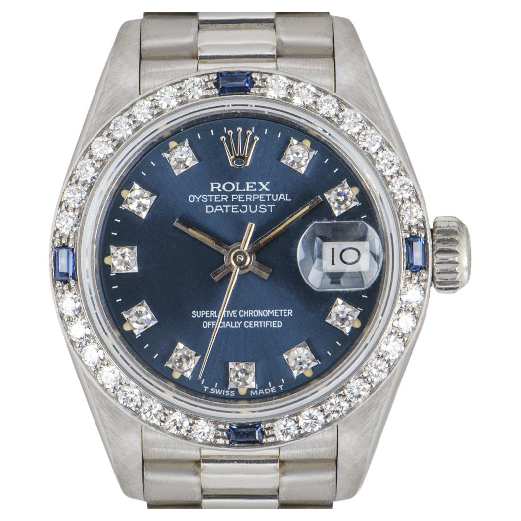A stunning 26mm Datejust crafted in white gold by Rolex. Featuring a blue dial that has a date display and is set with 10 round brilliant cut diamond hour markers. Complementing the dial is a white gold bezel set with 4 baguette cut blue sapphires