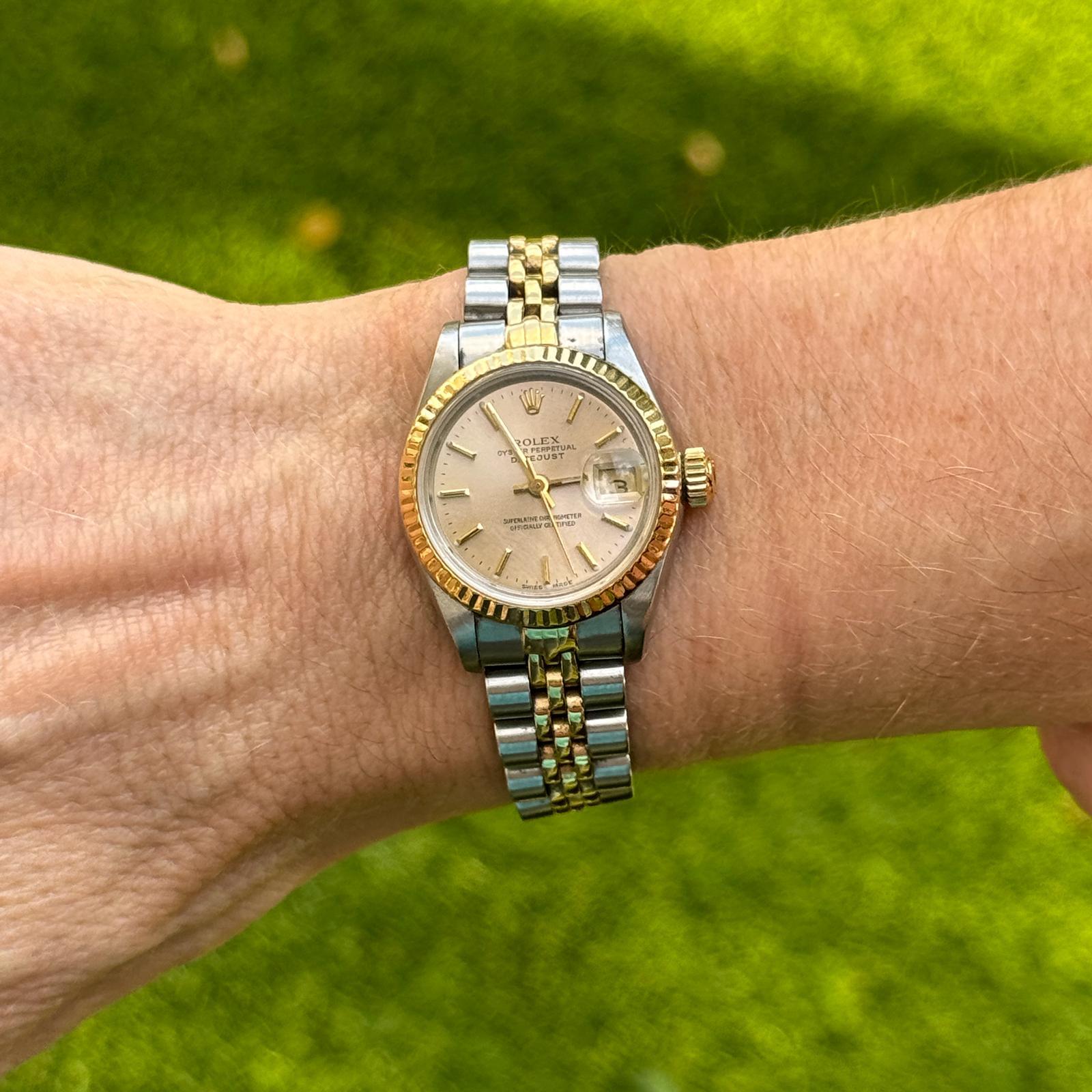 This elegant Rolex Lady-Datejust ref. 69173 features a 26mm stainless steel and 18K yellow gold case, complemented by a fluted bezel for a classic Rolex look. The silver dial offers a refined aesthetic with gold-tone hour markers and hands, ensuring
