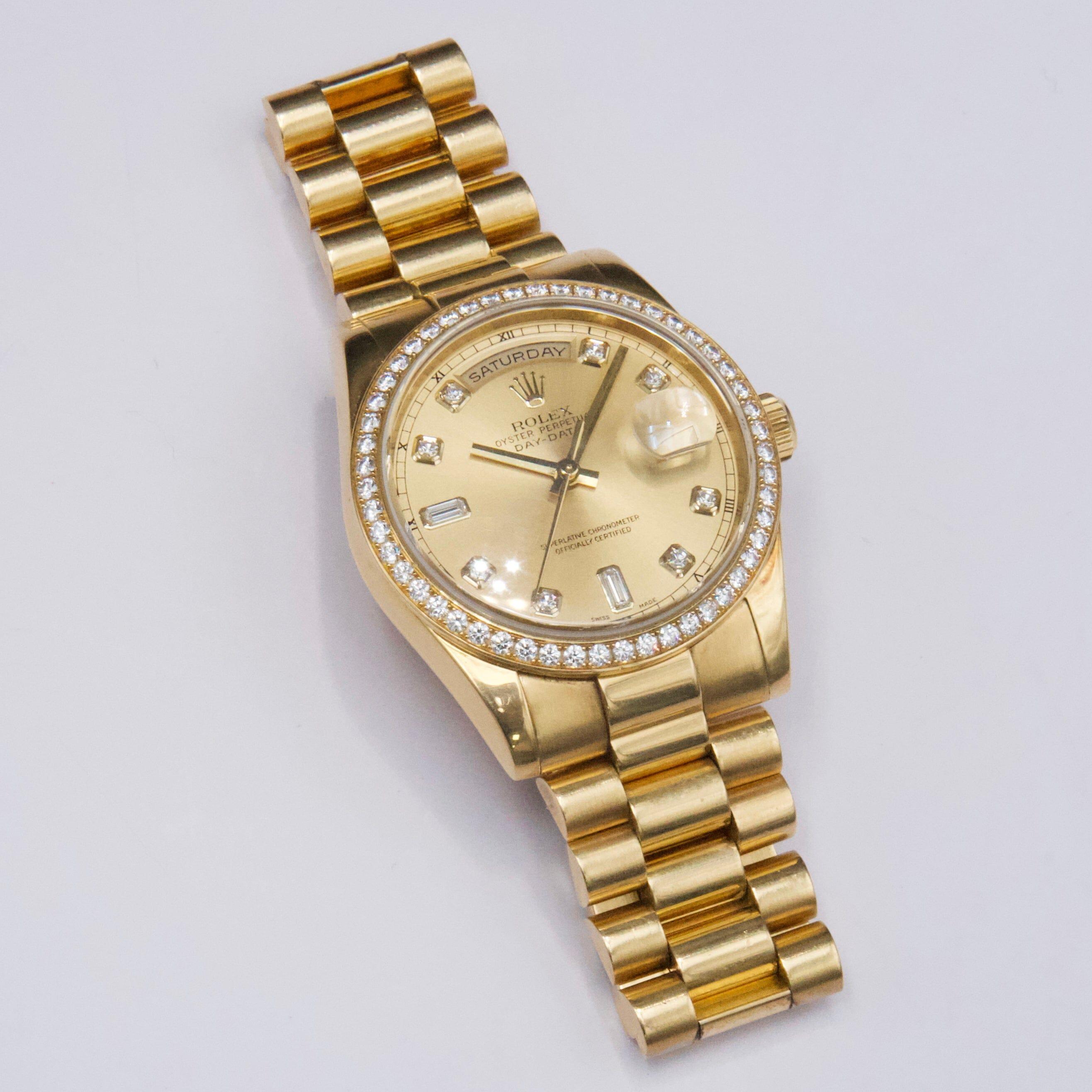 Reloj Rolex Day-Date 118348 para caballero. Caja de 36 mm de oro amarillo de 18 quilates. Bisel estriado de oro amarillo de 18 quilates con diamante de fábrica. Esfera de color champán con agujas doradas e índices de fábrica con diamantes. La fecha
